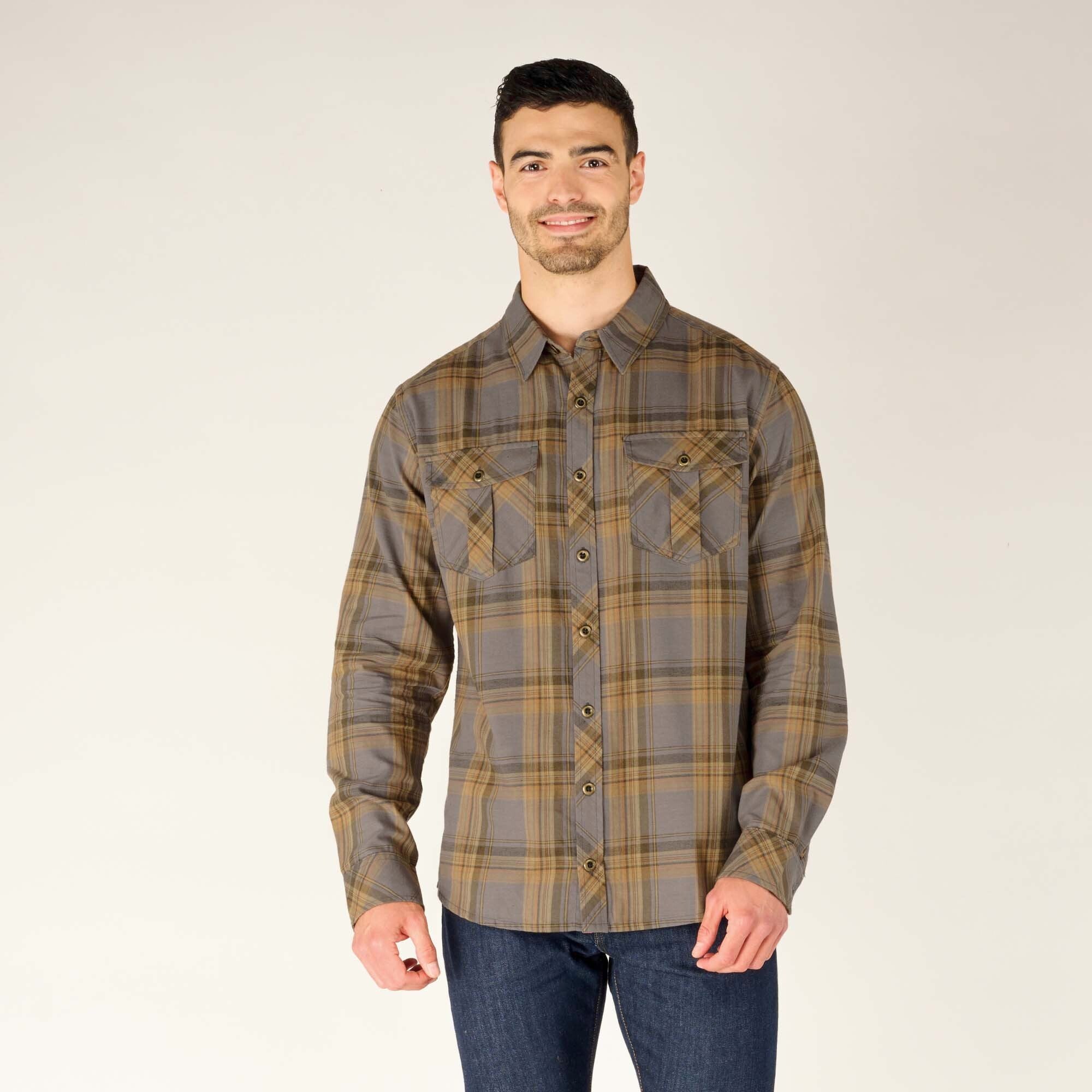 A model is wearing a Sherpa Adventure Gear Ramoche Shirt in Grey with dual button-flap chest pockets. The shirt is fully buttoned, showcasing a classic collar and tailored fit. The plaid pattern features thin mustard lines interwoven with wider grey stripes, creating a subtle yet bold aesthetic. The model pairs the shirt with dark blue jeans, smiling and standing against a neutral background.