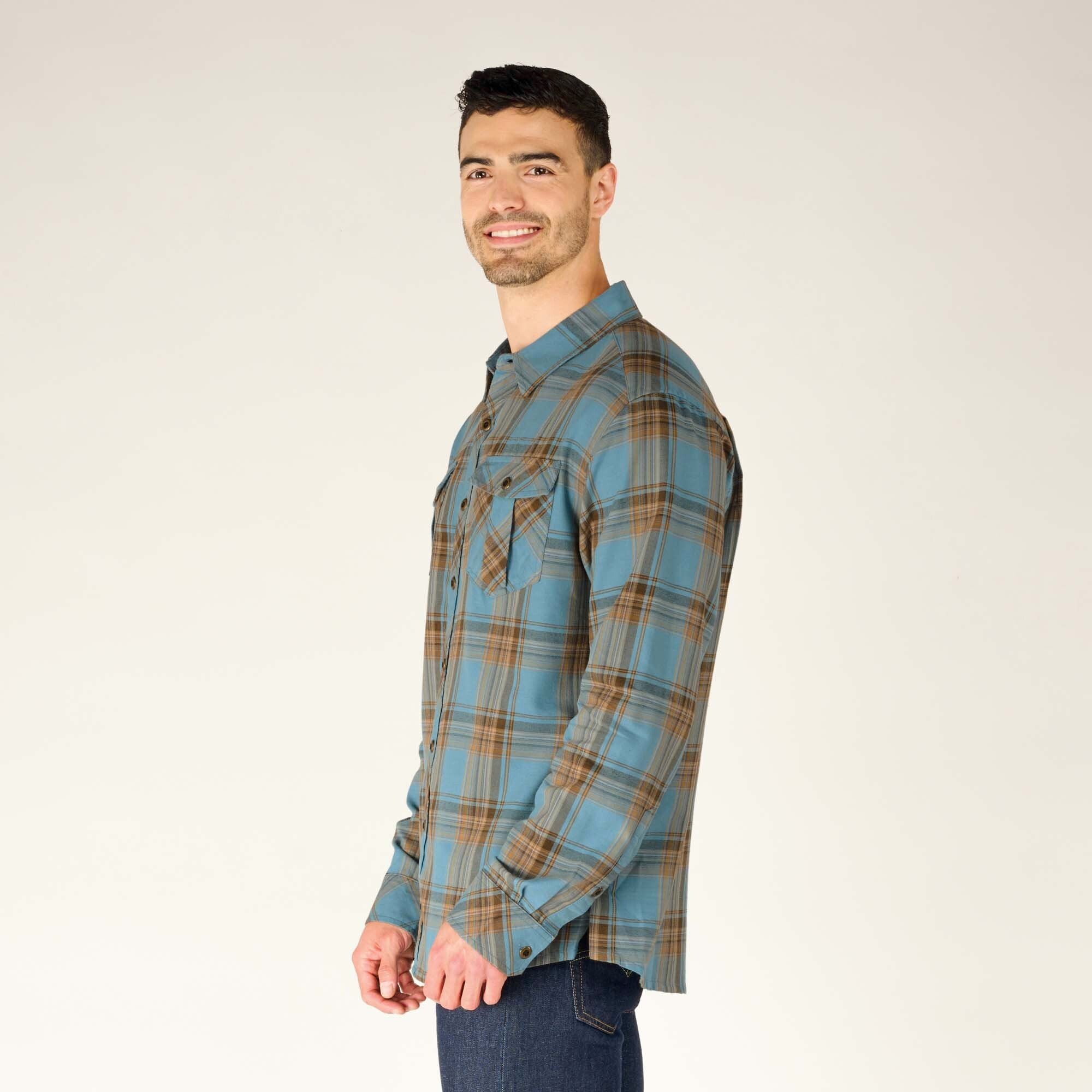 A profile view from the left side of the model, showing the sleeve fit and the structure of the Sherpa Adventure Gear Ramoche Shirt in Grey's collar and chest pocket detailing. The model smiles as he slightly tilts his head, maintaining a casual stance.