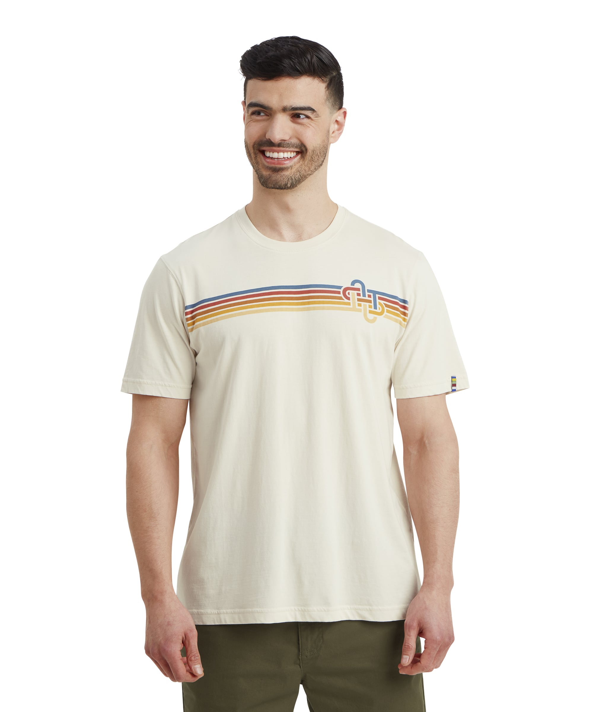 A smiling man wearing a Sherpa Adventure Gear Retro Knot T-Shirt in White with a colorful retro-inspired horizontal stripe design across the chest in shades of yellow, orange, and blue. The t-shirt features a knot-like logo on the left chest. The man is standing in a relaxed pose with his arms at his sides.