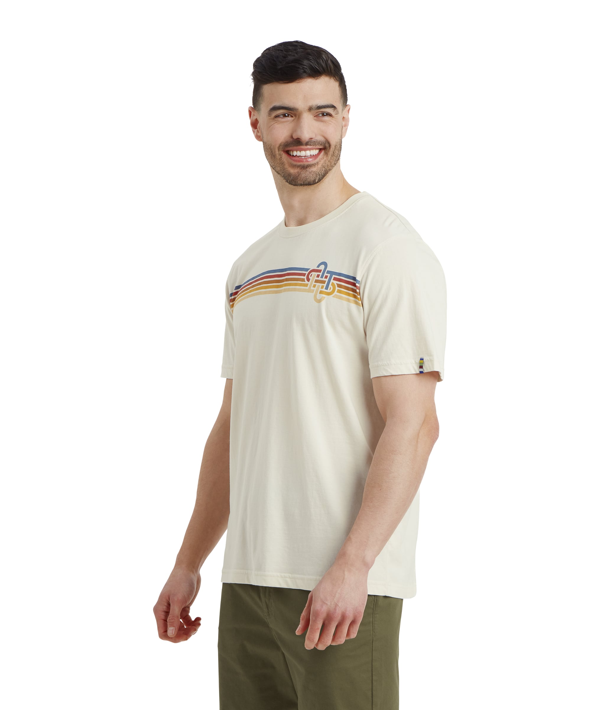 A side-profile view of the man wearing the Sherpa Adventure Gear Retro Knot T-Shirt in White with the colorful stripe design and olive-green shorts. He is smiling and looking forward, showcasing the t-shirt's relaxed fit.