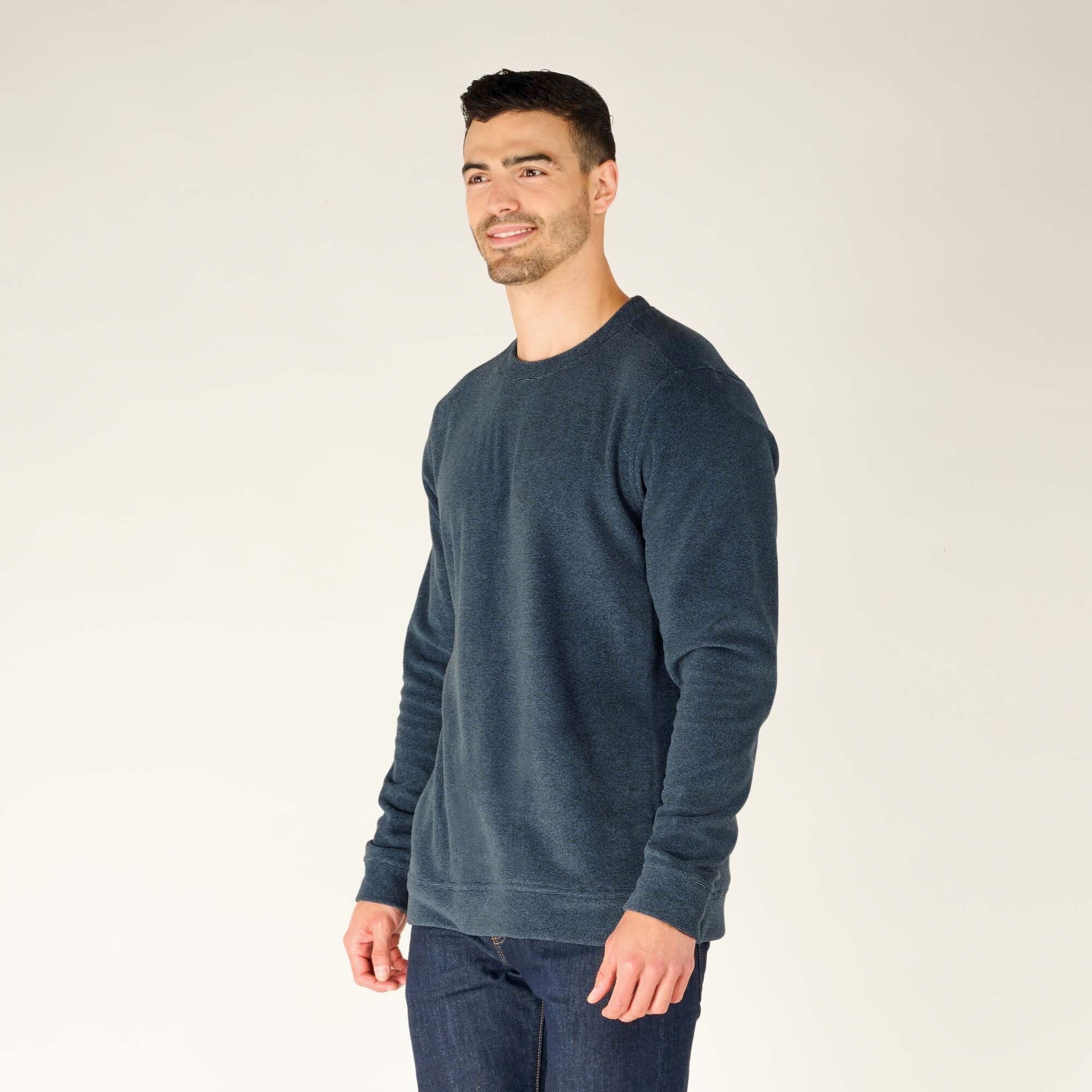 The model is shown in a three-quarter view, looking slightly off to the side while wearing the Sherpa Adventure Gear Rolpa Crew in Blue. The crewneck sweater’s rich blue color and soft brushed fleece texture are visible. The fit is slightly relaxed, with the hem sitting just below the waist and the cuffs gently hugging the wrists. The plain white backdrop keeps the focus on the garment.