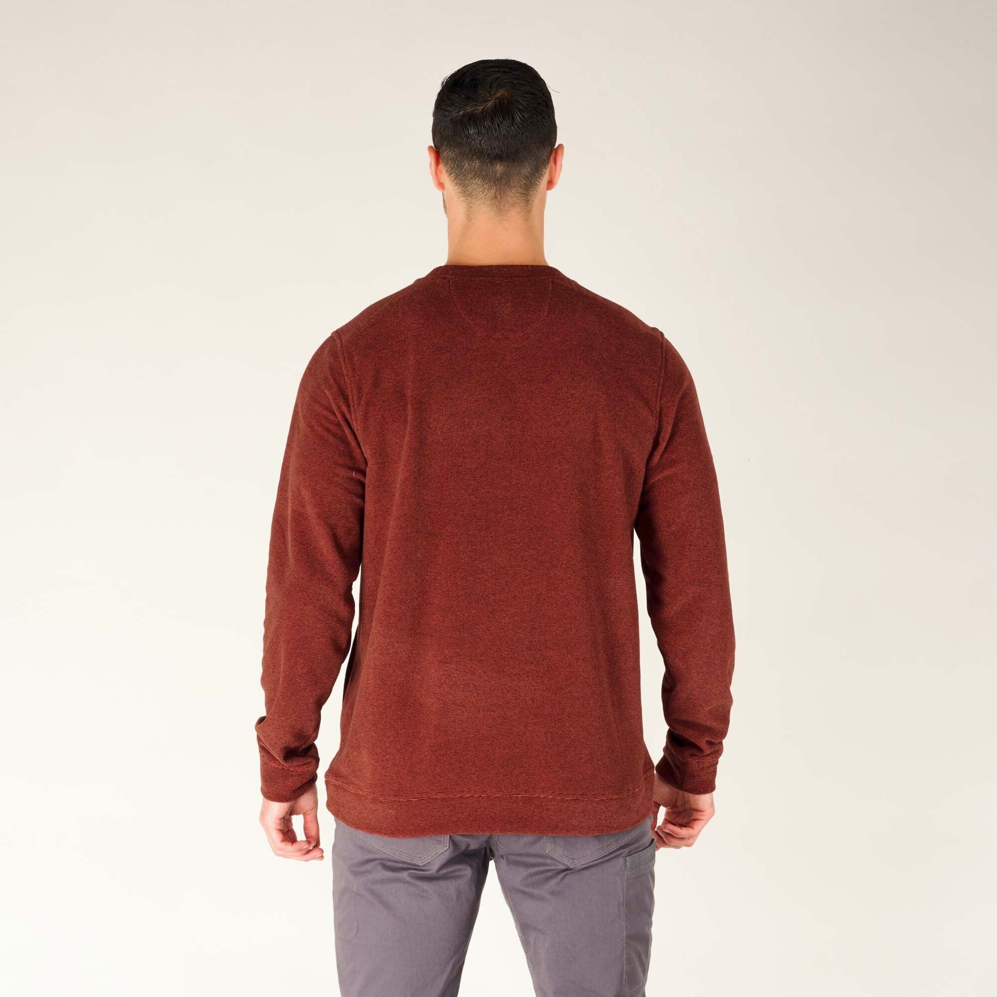 The model is photographed from the back, showcasing the rear view of the Sherpa Adventure Gear Rolpa Crew in Red. The heathered fabric is visible across the entire back panel. The fit is slightly loose, with the hem falling just below the waist. The ribbed cuffs and hem maintain the structured fit.