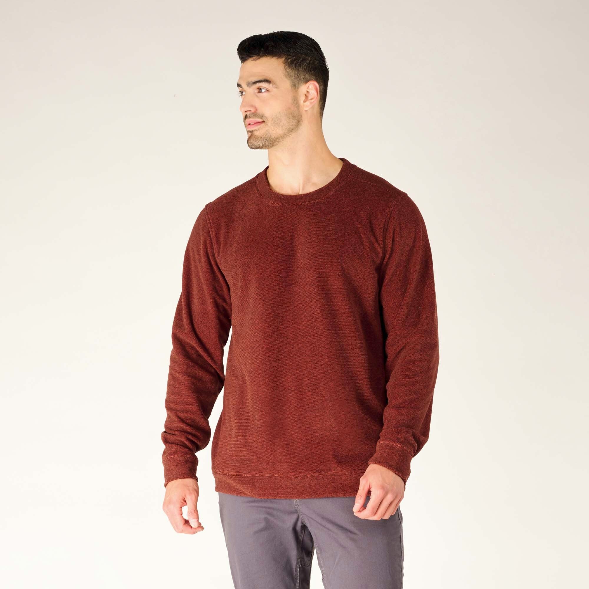 The model stands at a slight angle, turning his head to the side while wearing the Sherpa Adventure Gear Rolpa Crew in Red. This position highlights the crewneck collar, which sits flat and smooth, and the fit across the chest and shoulders. The heathered fabric texture is evenly distributed across the garment, giving it a casual yet refined look.