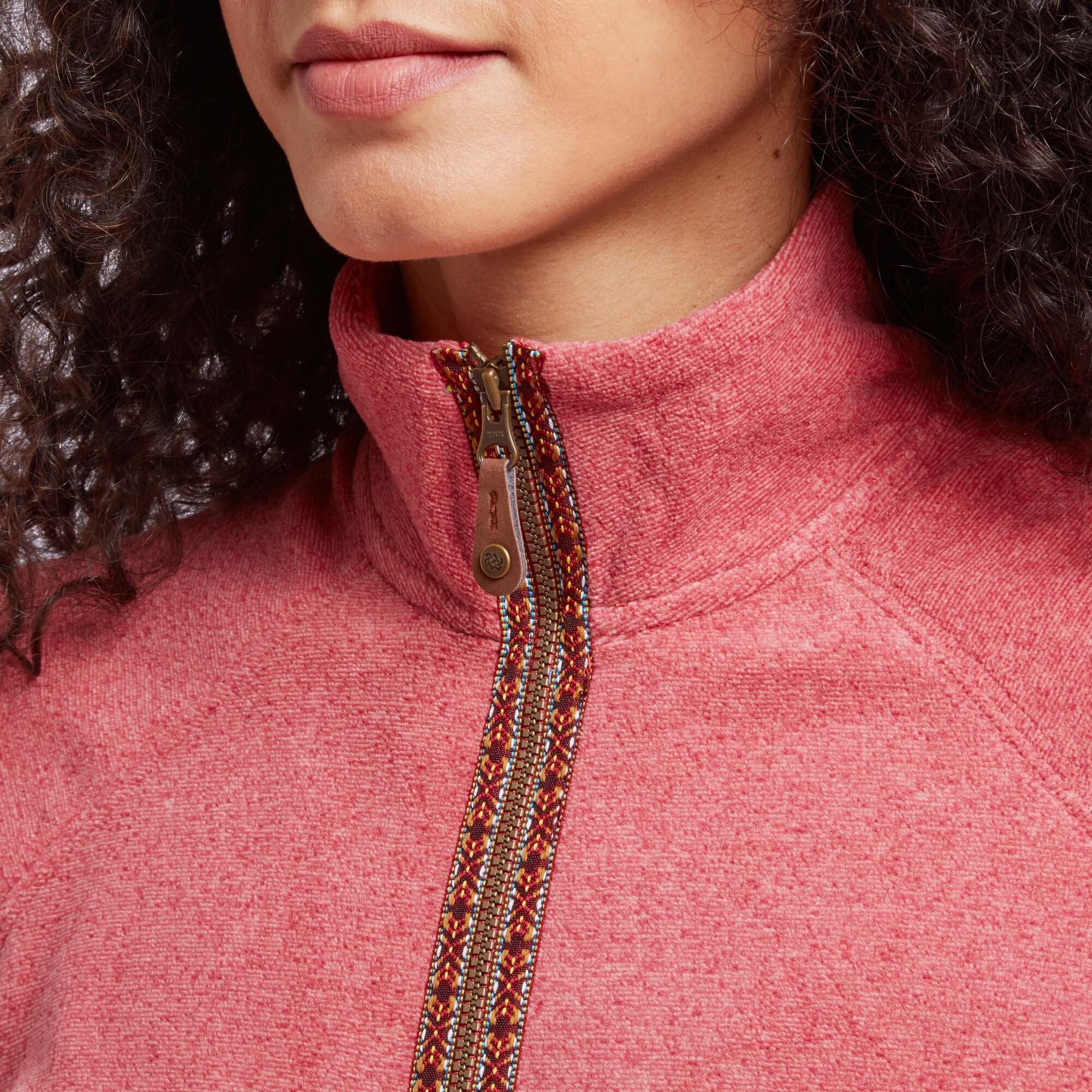 Close-up of the Sherpa Adventure Gear Rolpa Eco Jacket in Red's zipper and collar. The zipper features a patterned trim in vibrant colors and a brass zipper pull with Sherpa branding. The high collar provides additional warmth.