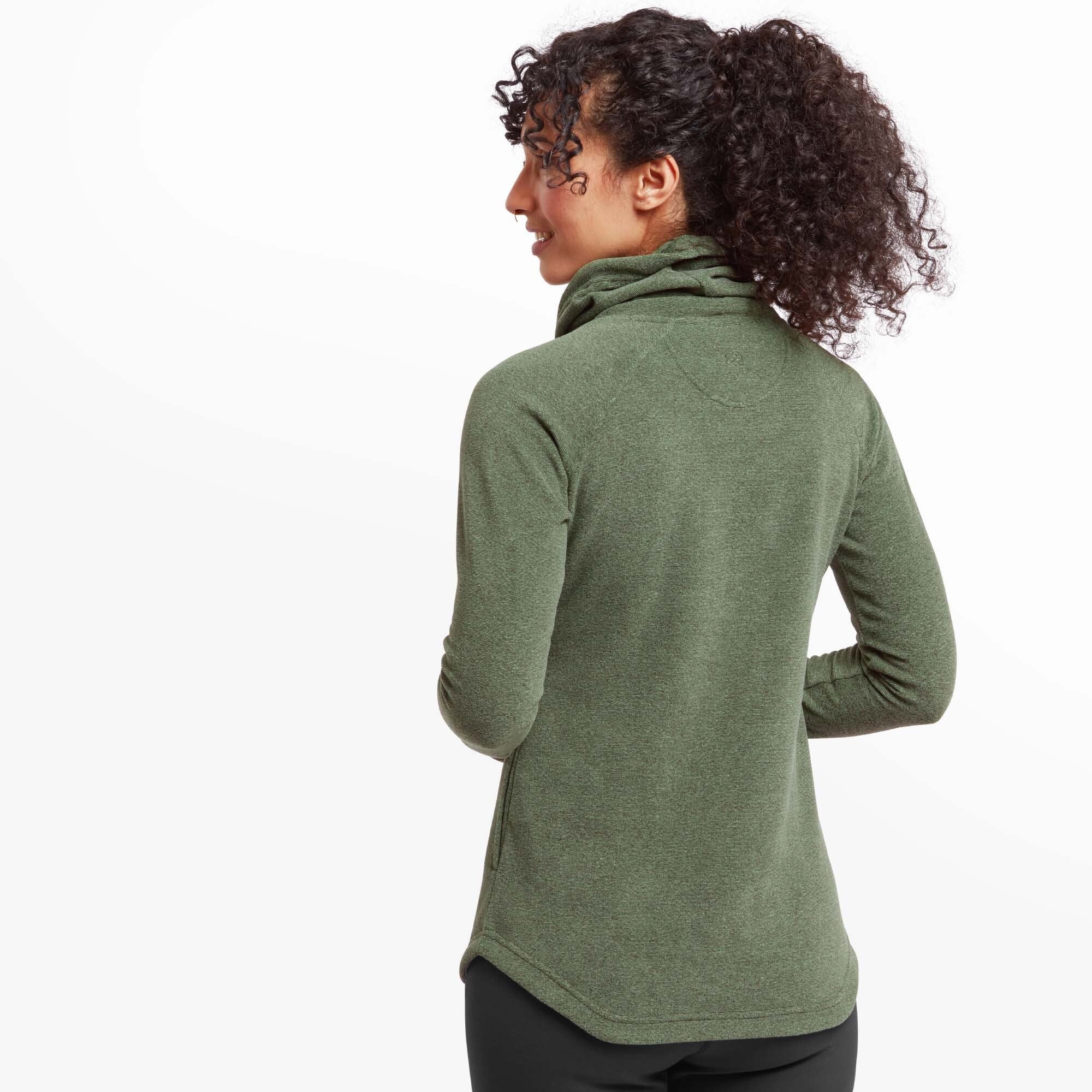 Rear view of the woman in the Sherpa Adventure Gear Rolpa Eco Pullover in Green, showing the curved hem at the back and subtle seam details across the shoulders. Her curly hair is tied back in a high ponytail, and she is looking over her shoulder with a smile.