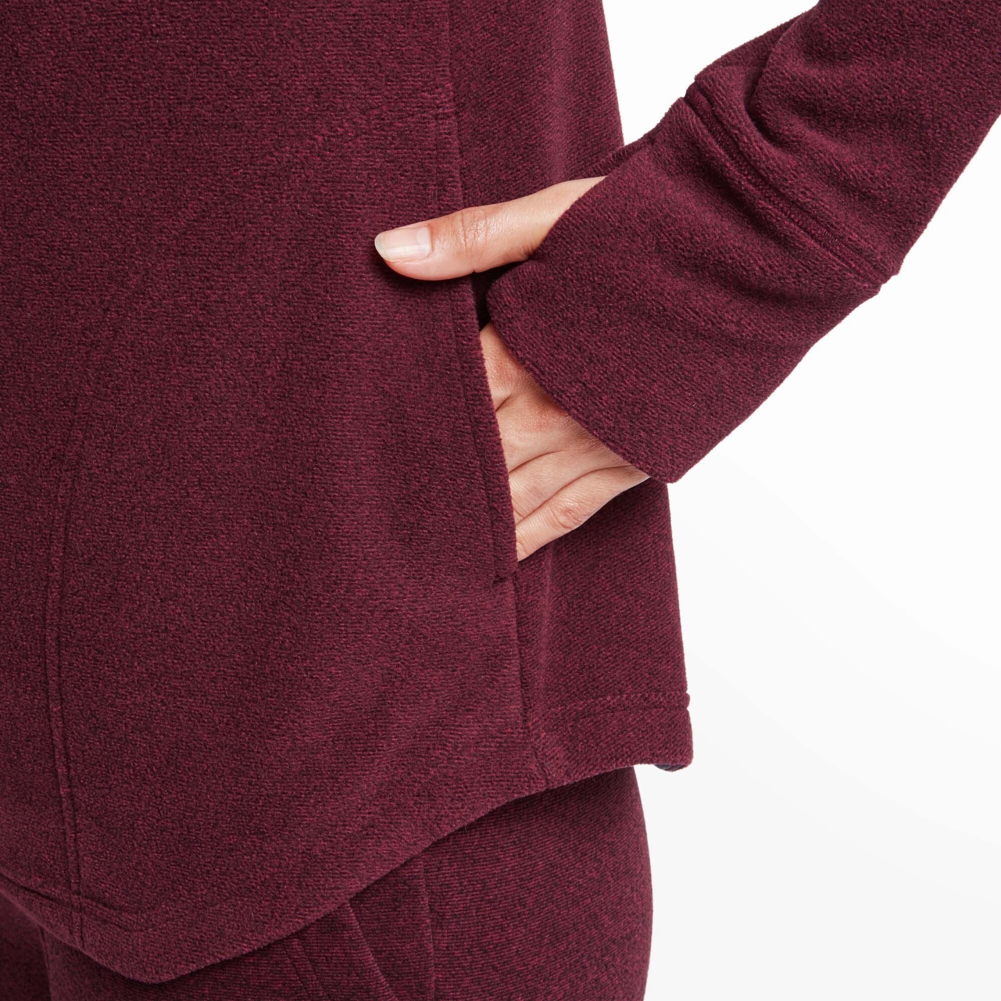 A close-up shot captures the model’s hand tucked into the side pocket of the Sherpa Adventure Gear Rolpa Eco Pullover in Red, showing the soft fleece-like texture of the fabric. The seam detailing around the pocket and the extended cuff with a thumbhole are also visible.