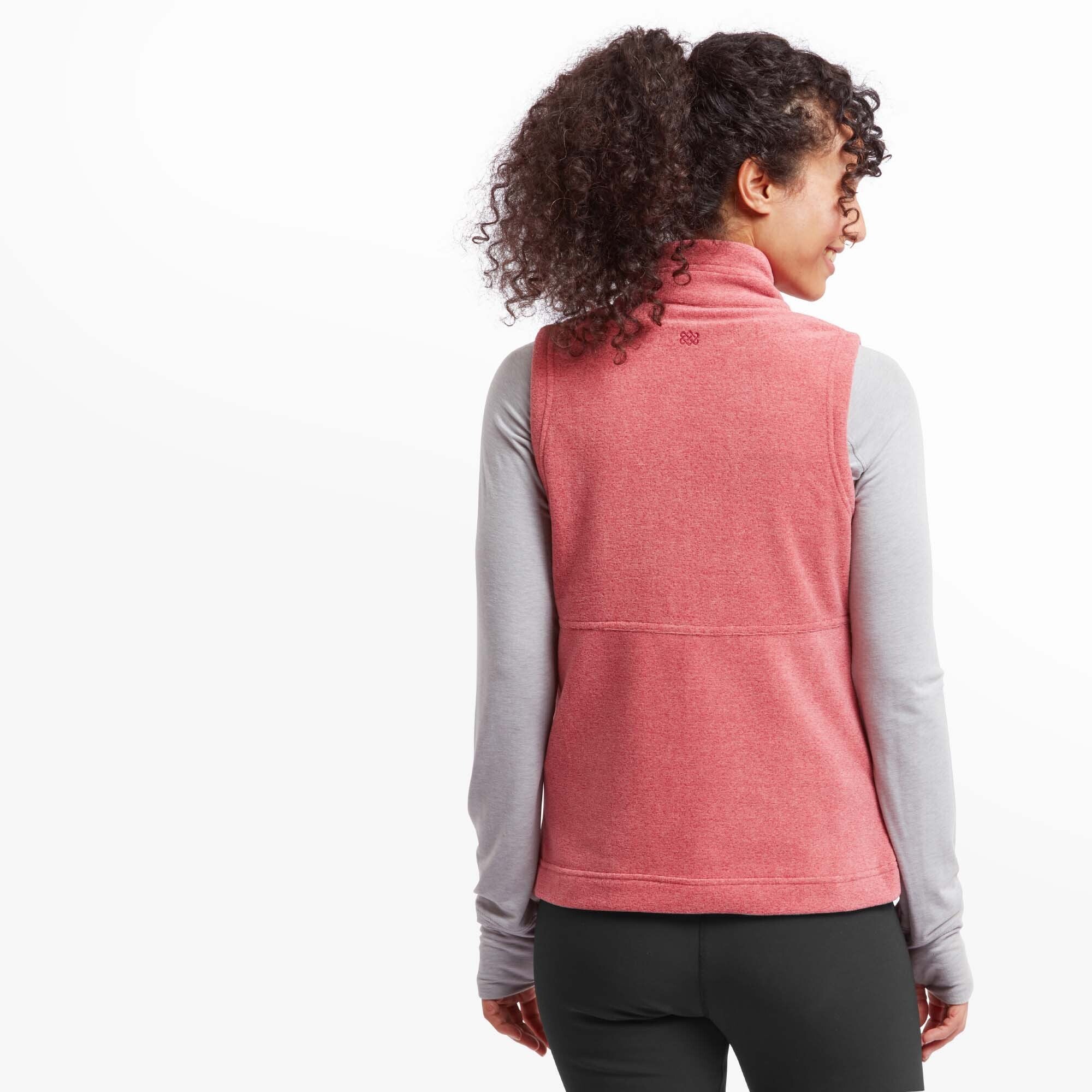 A back view of the Sherpa Adventure Gear Rolpa Eco Vest in Red, highlighting its clean, simple design and the small embroidered logo detail at the top of the back panel. The vest contours well around the shoulders, and the model's hair is tied back in a high ponytail for a sporty look.