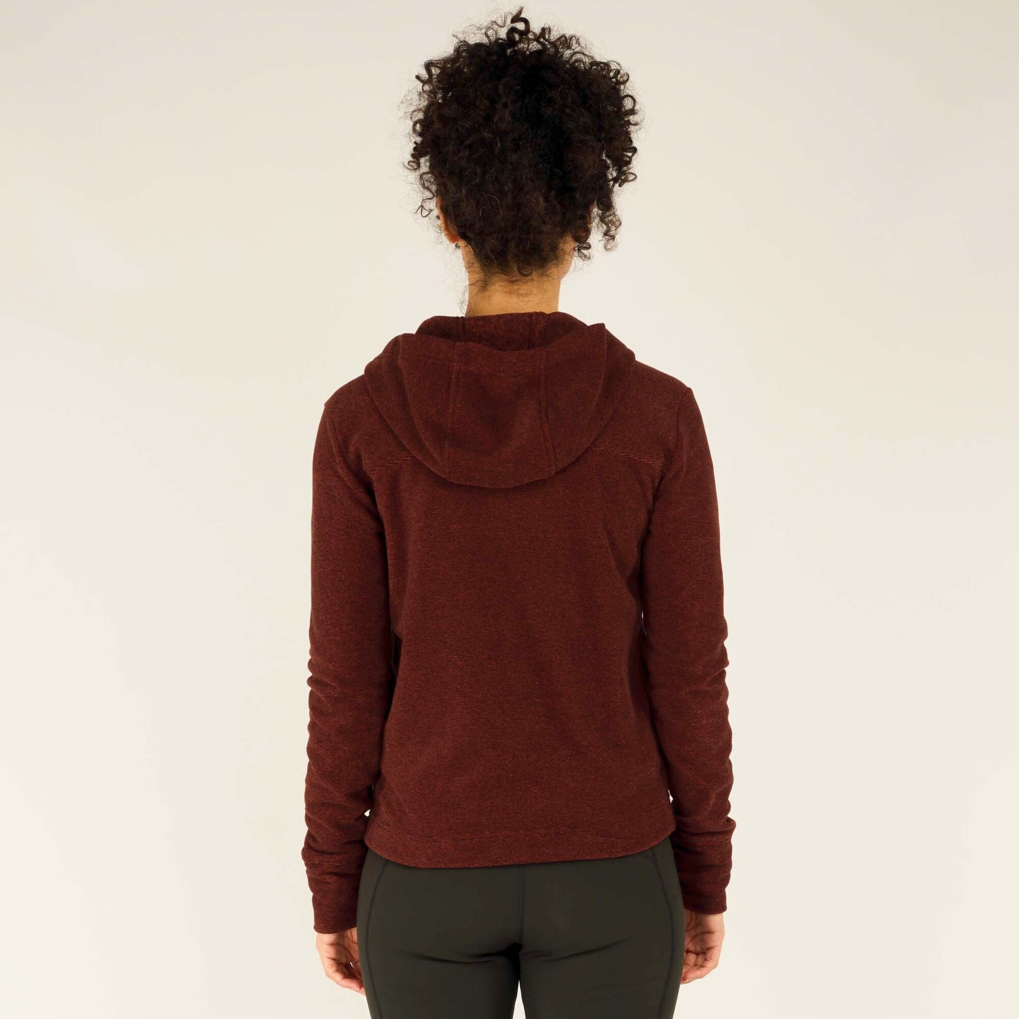 Side profile of the model wearing the Sherpa Adventure Gear Rolpa Full Zip Hoodie in Red. The hood is draped down the back, revealing the seam construction along the shoulders. The slightly relaxed fit is noticeable, and the side view highlights how the hoodie contours to the body while maintaining a comfortable fit.