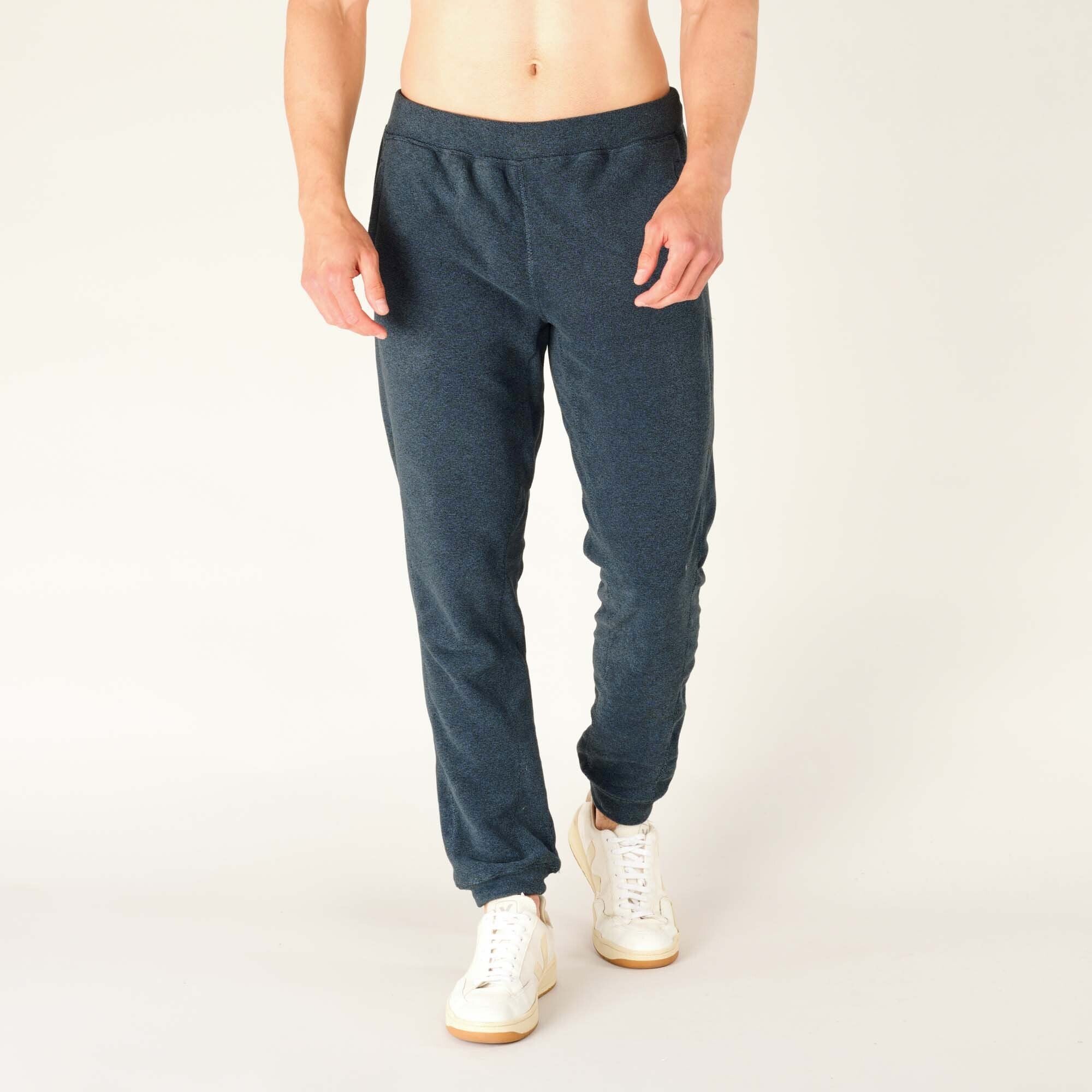 Front view of a male model wearing Sherpa Adventure Gear Rolpa Jogger in Blue. The joggers have a soft fleece-like texture, an elastic waistband, and relaxed tapered fit ending in cuffed ankles. The model is barefoot, showing the natural fit at the bottom.