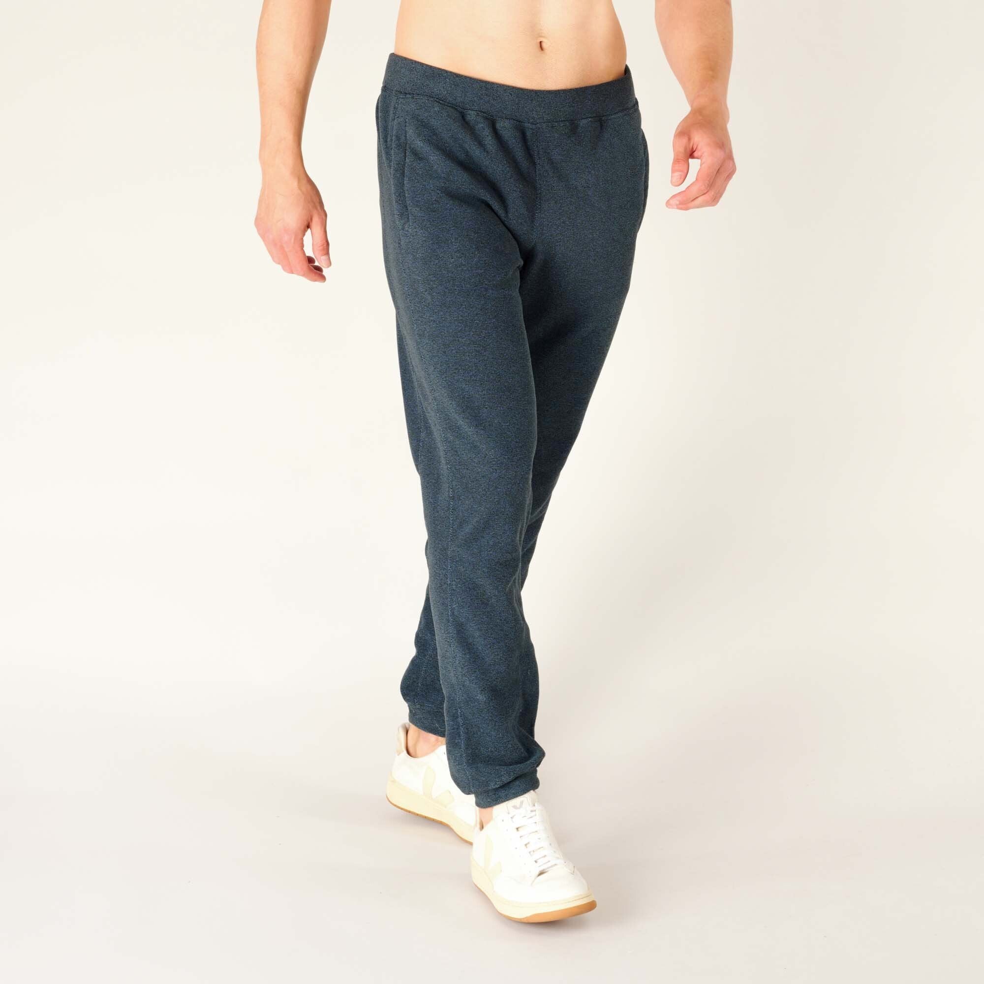 Side walking view of the model wearing the Sherpa Adventure Gear Rolpa Jogger in Blue, showing the slight stretch and drape of the fabric in motion. The pockets blend into the seams, and the soft fabric highlights its casual, cozy style.