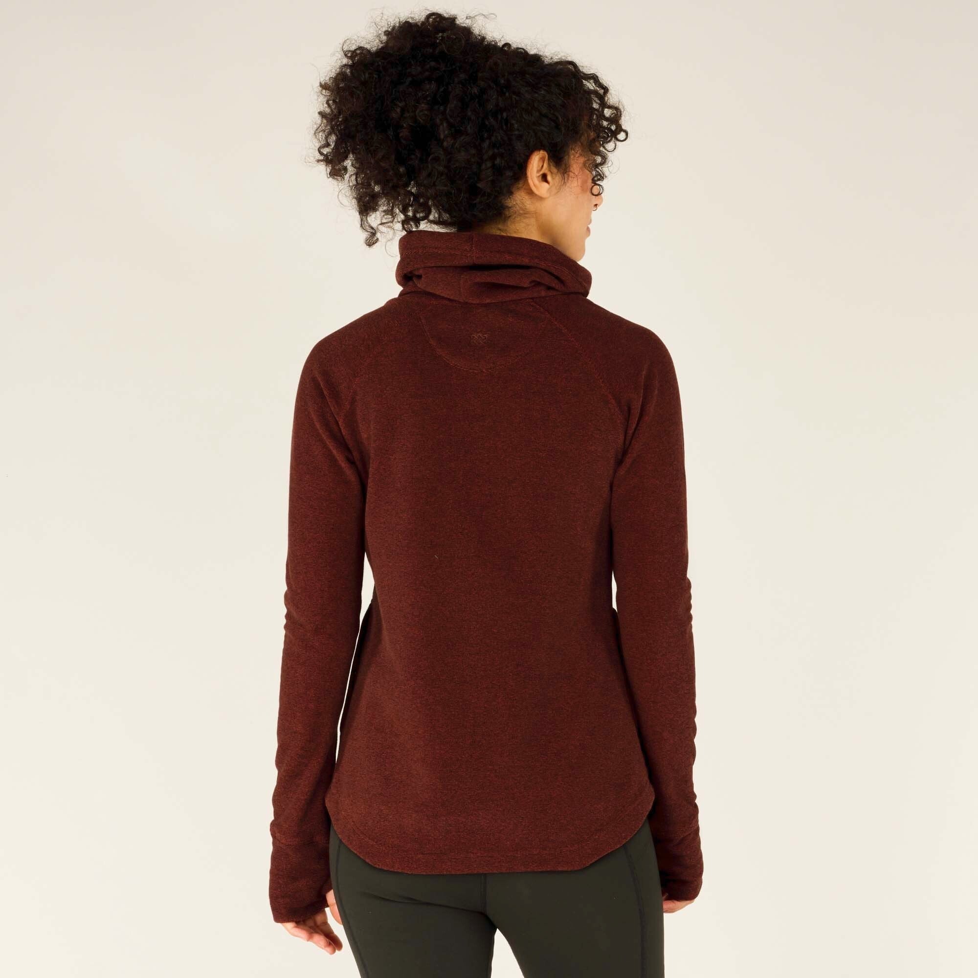 The back view of the Sherpa Adventure Gear Rolpa Pullover in Red showcases the raglan sleeve design and the gently curved hemline. The fabric appears slightly marled, adding visual interest. The fit is relaxed but flattering, sitting comfortably over the leggings.