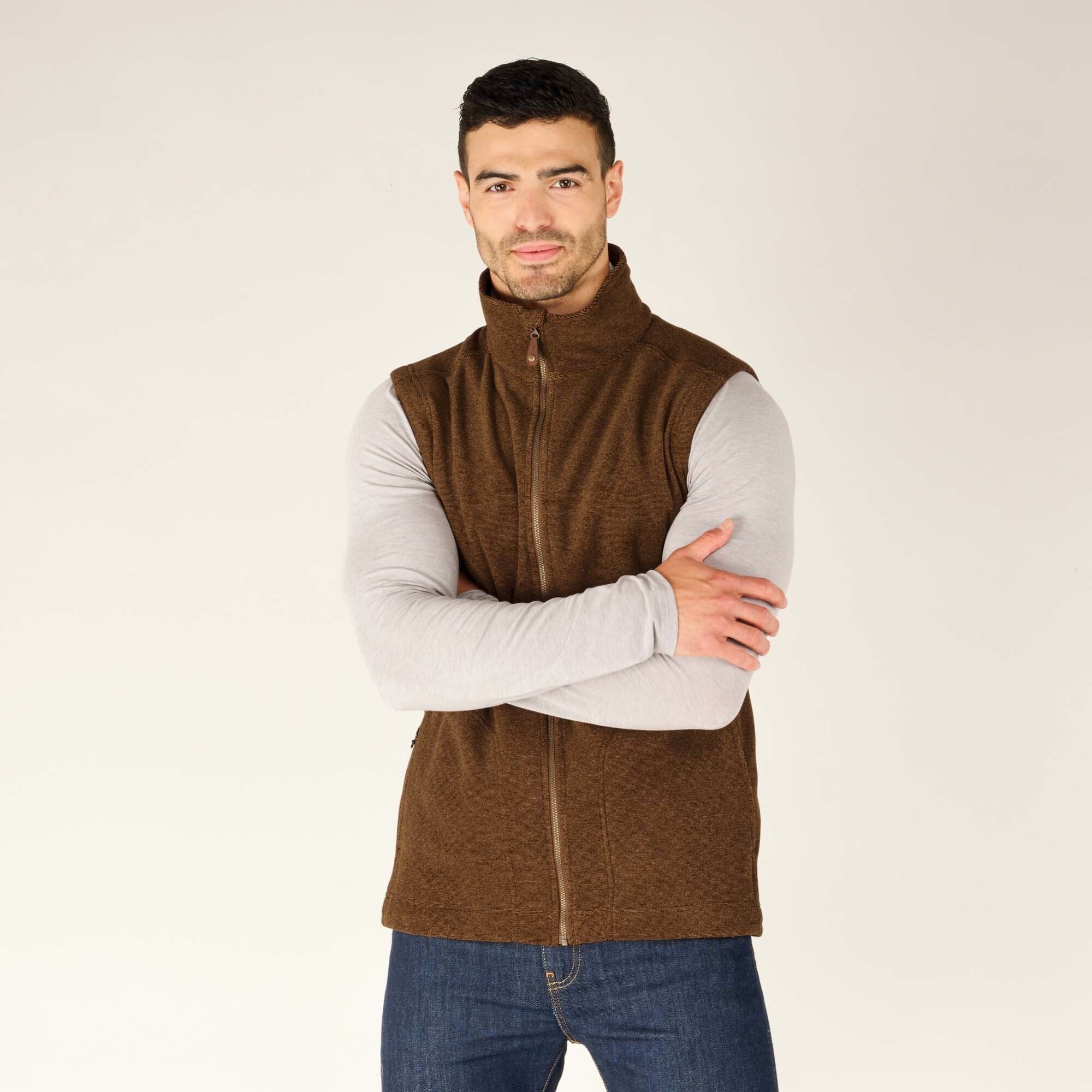 The same model wearing the Sherpa Adventure Gear Rolpa Vest in Light Brown. He is standing with his arms crossed and smiling slightly. The texture of the vest's fabric and its clean stitching are clearly visible.