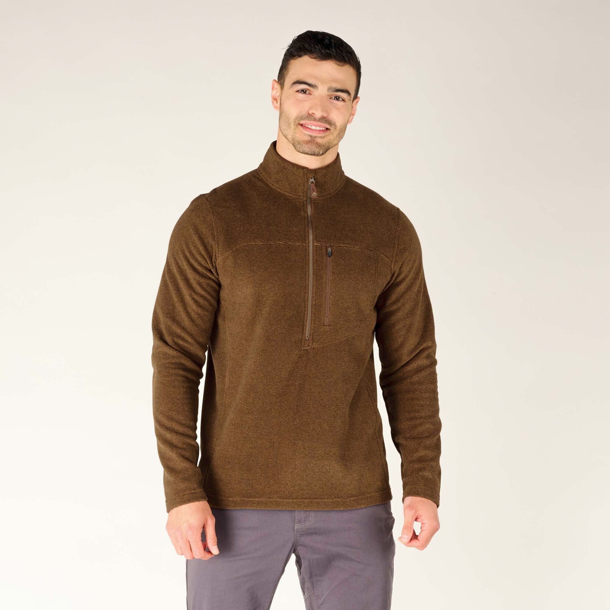 The male model stands facing the camera, wearing the Sherpa Adventure Gear Rolpa Zip T-Shirt in Light Brown fully zipped up to the collar. The chest pocket zipper is visible, and the long sleeves have a slim fit. His hands are relaxed at his sides, and he has a slight smile.