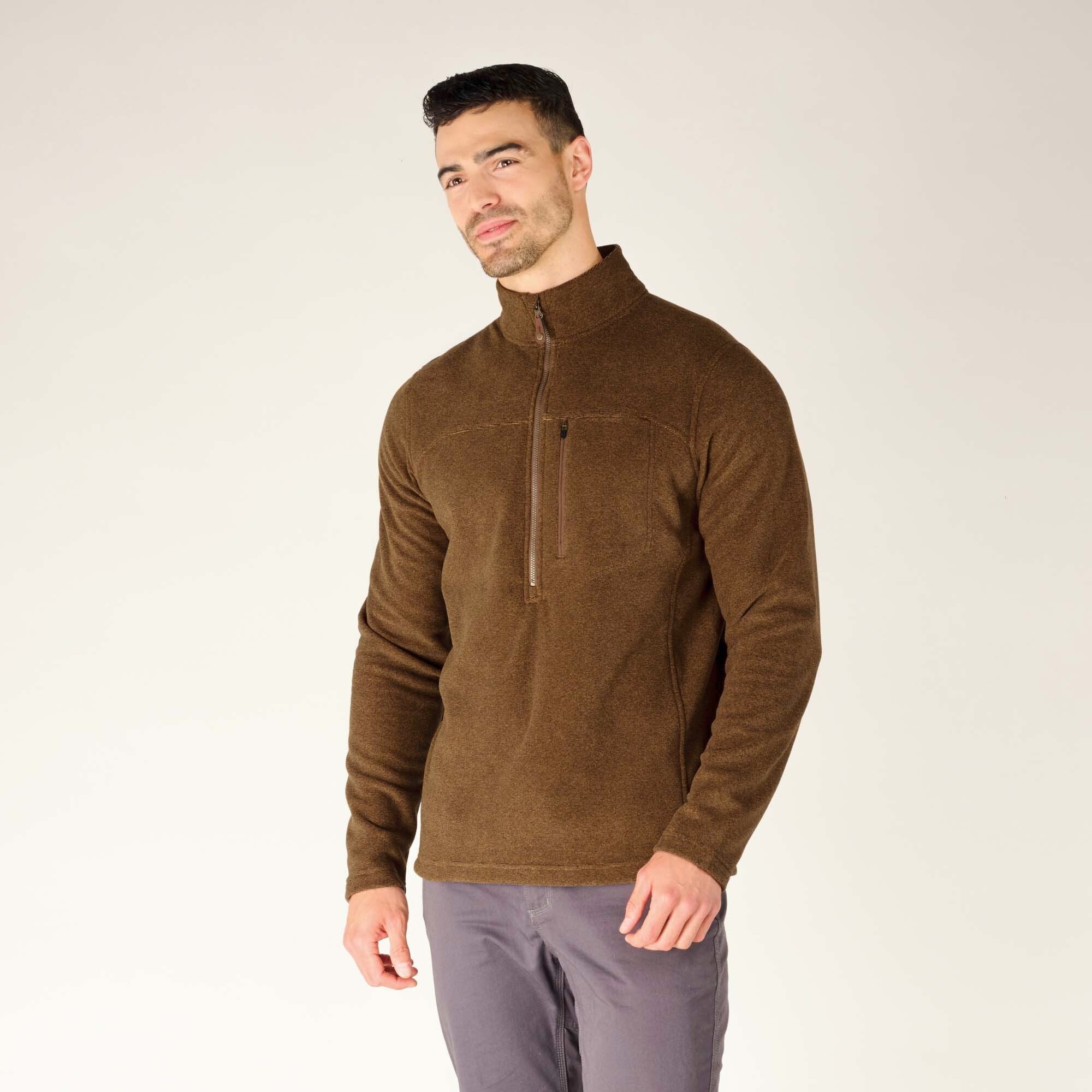 The male model poses at a slight angle, showcasing the front and side profile of the Sherpa Adventure Gear Rolpa Zip T-Shirt in Light Brown. His head is turned slightly to the side, with a soft smile. The chest pocket and zip detail are clearly visible.