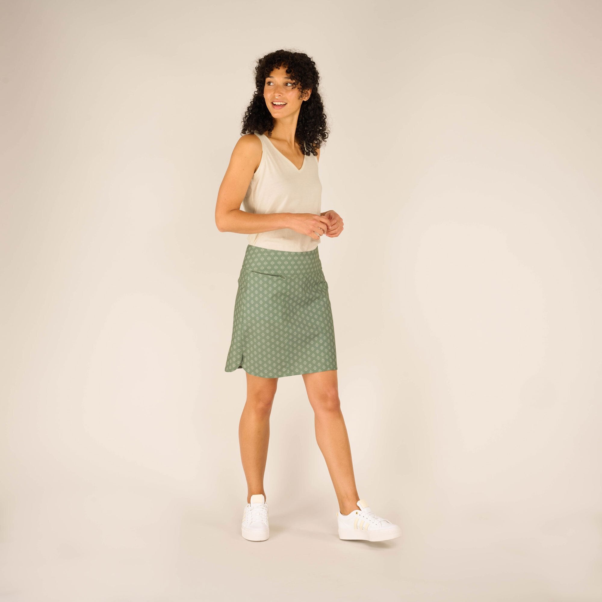 A side view of the Sherpa Adventure Gear Sajilo Adventure Skort in Green worn by the model, highlighting the smooth fit around the waist and hips, complemented by the comfortable fabric and casual white trainers.