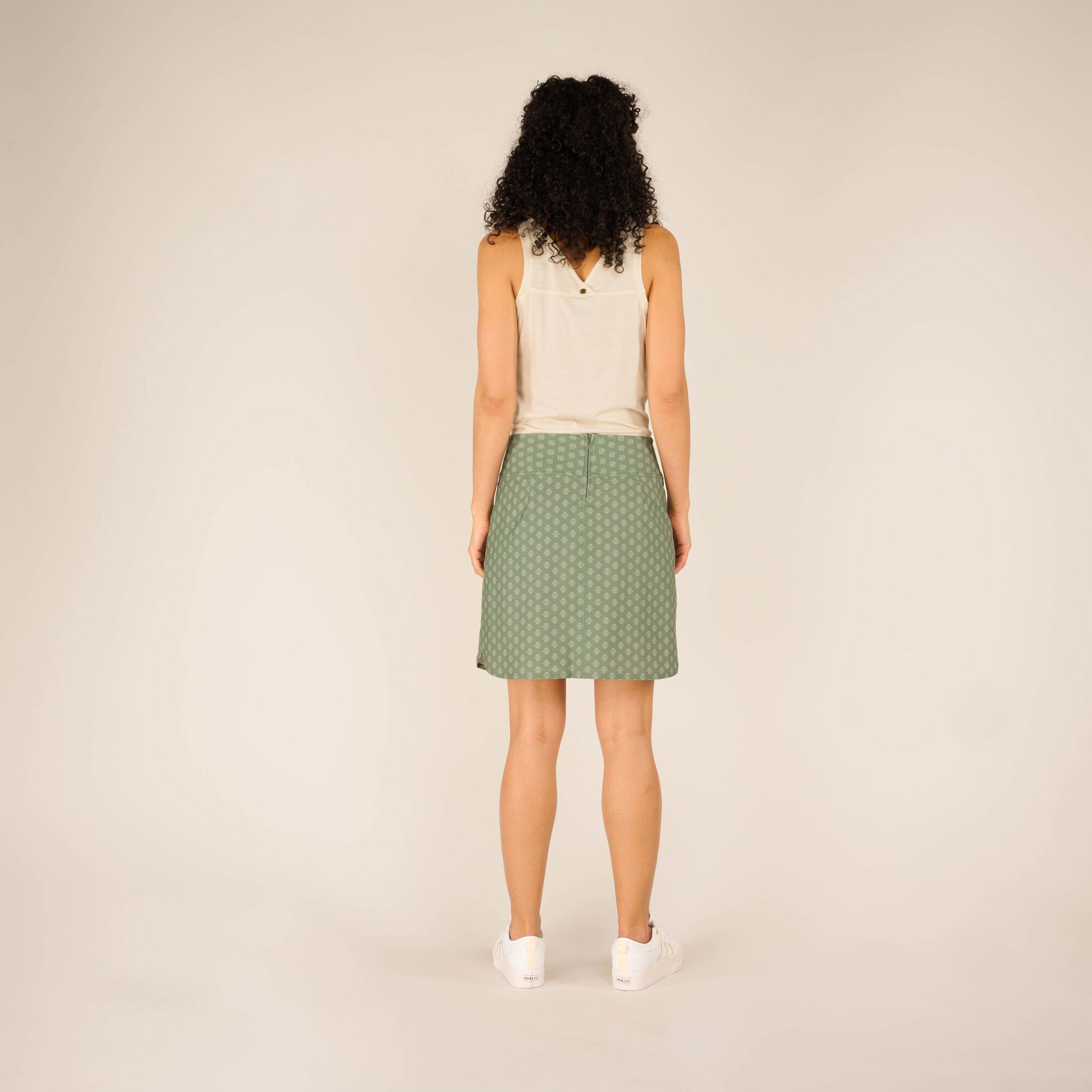 A view of the sSherpa Adventure Gear Sajilo Adventure Skort in Green from behind, showcasing the back zipper closure and the overall fit, paired with the same sleeveless top and white trainers.