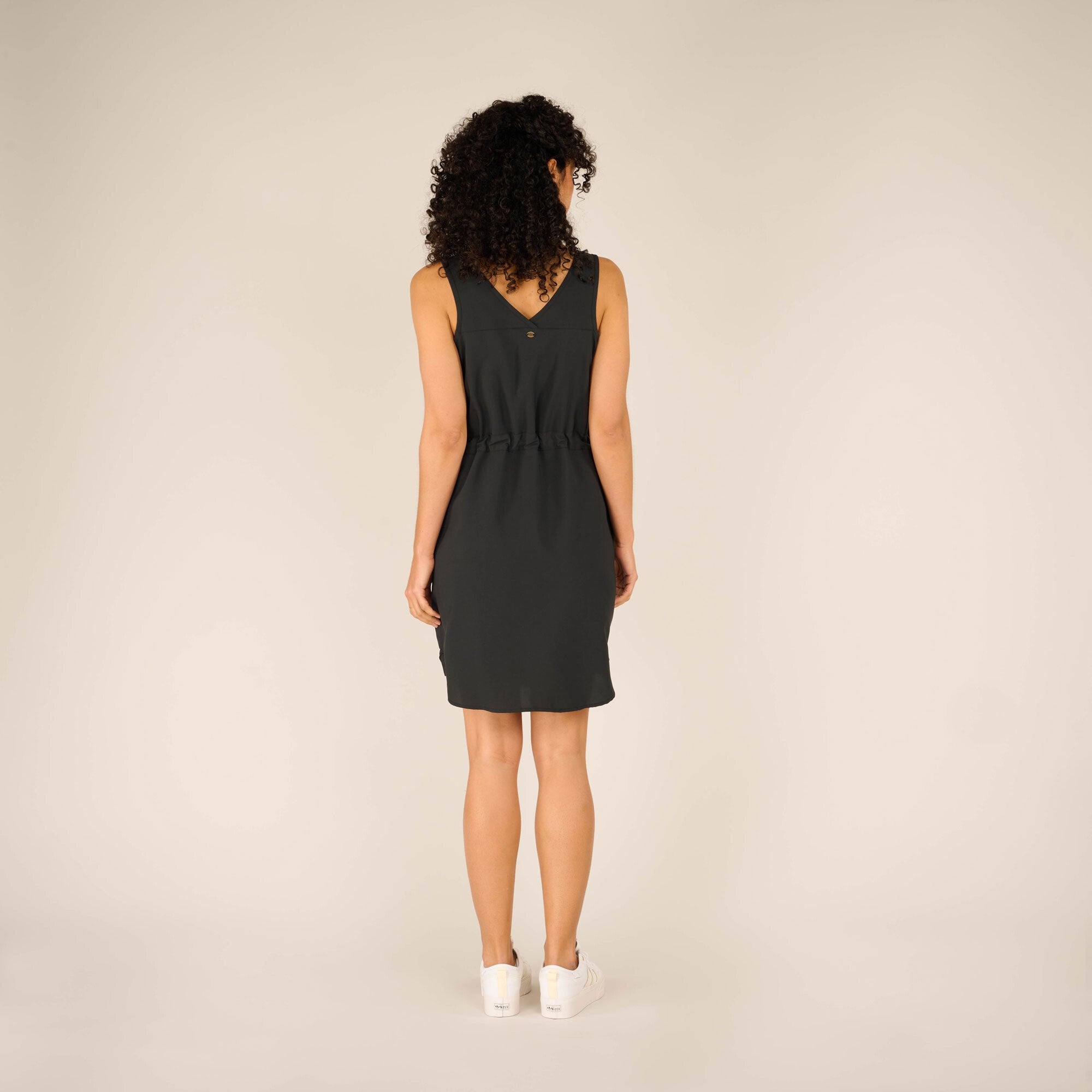 A rear view of the Sherpa Adventure Gear Sajilo Dress in Black highlighting its V-shaped back detail with a subtle decorative button at the center. The dress falls just above the knees, creating an effortless and chic look.