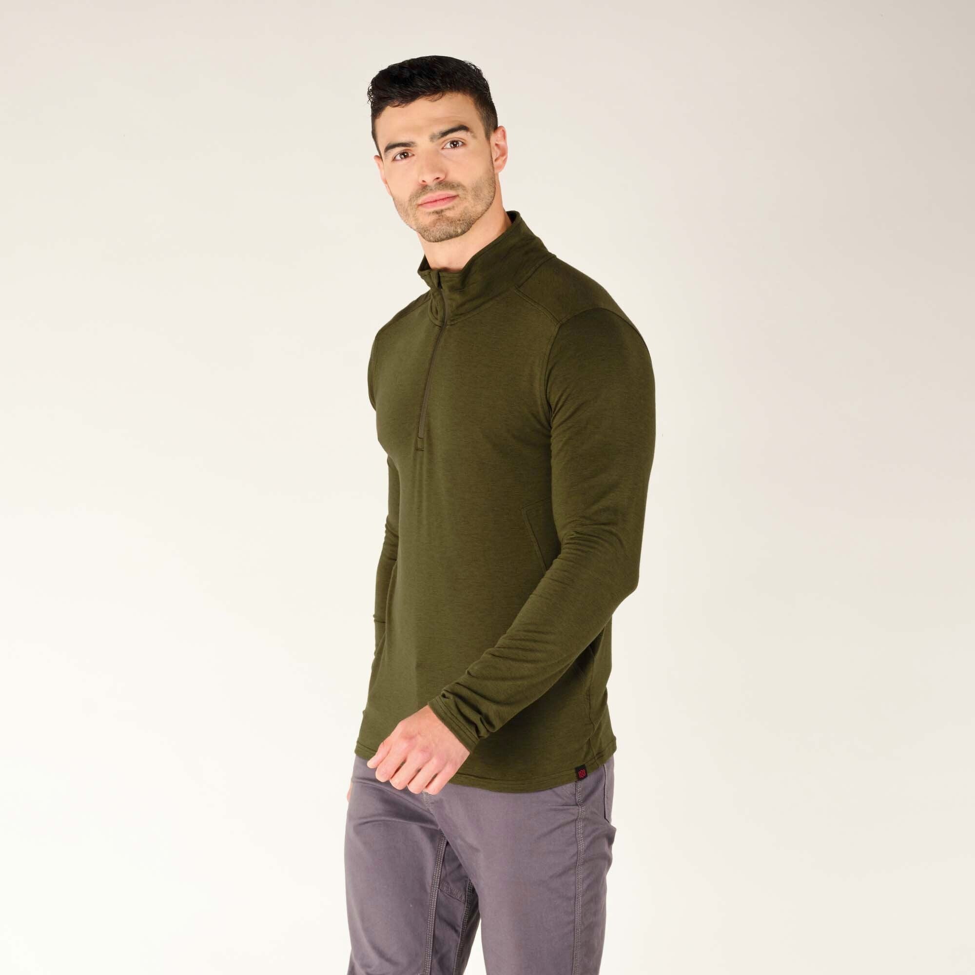 The model is now turned around, facing away from the camera. The back view of the Sherpa Adventure Gear Tendu Active Half Zip in Green is visible, displaying subtle seam details on the shoulders and back panel. His posture is upright with relaxed shoulders and his arms naturally resting at his sides.