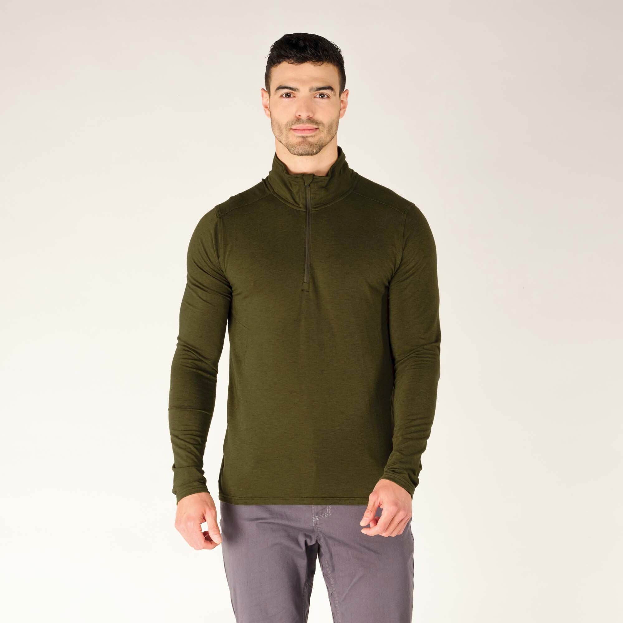 A front-facing, full-body shot of the model, standing straight with his hands at his sides. The Sherpa Adventure Gear Tendu Active Half Zip in Green’s minimalistic design is highlighted, with clean lines and a smooth texture. The zipper is fully zipped, covering his neck, and he has a confident expression.