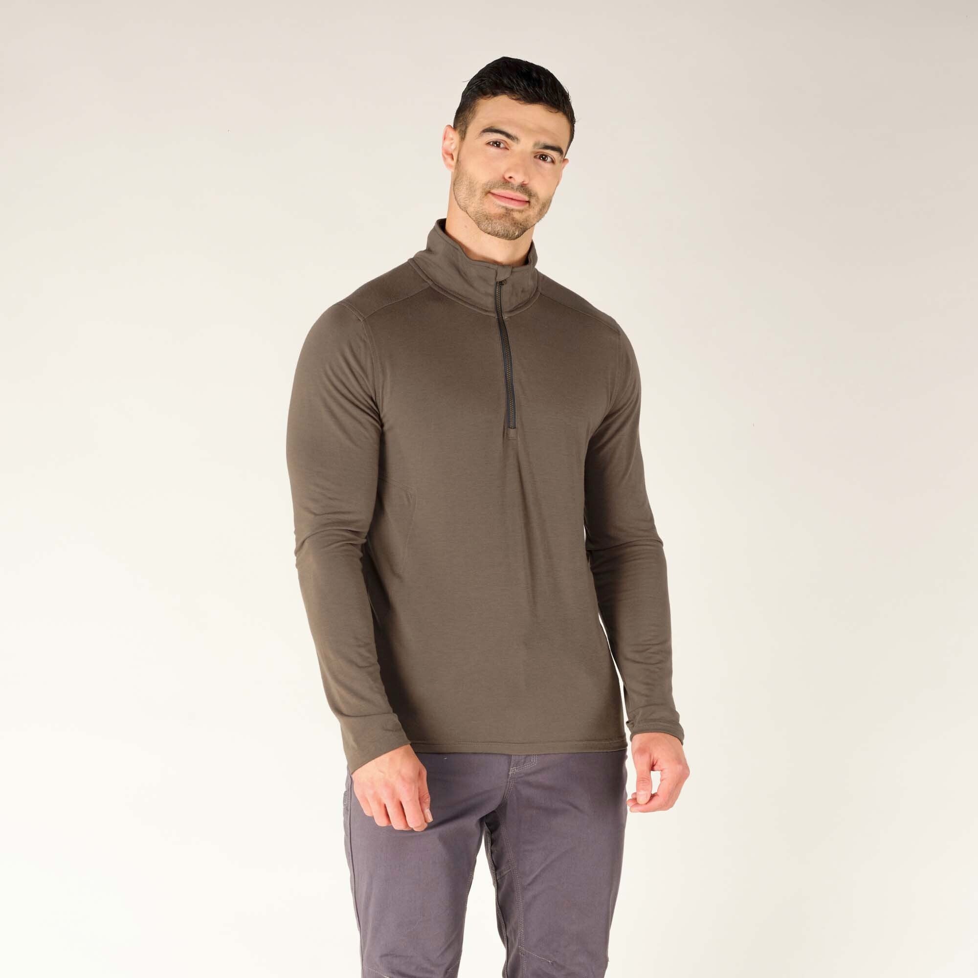 The same male model is shown in a slight turn, giving a three-quarter front view of the Sherpa Adventure Gear Tendu Active Half Zip in Grey. This angle highlights the contouring fit around the torso and arms, emphasizing the athletic cut of the garment. The high collar remains zipped up, and the model’s expression is soft with a slight smile. The lightweight, breathable texture of the fabric is visible, indicating its purpose as a performance layer.