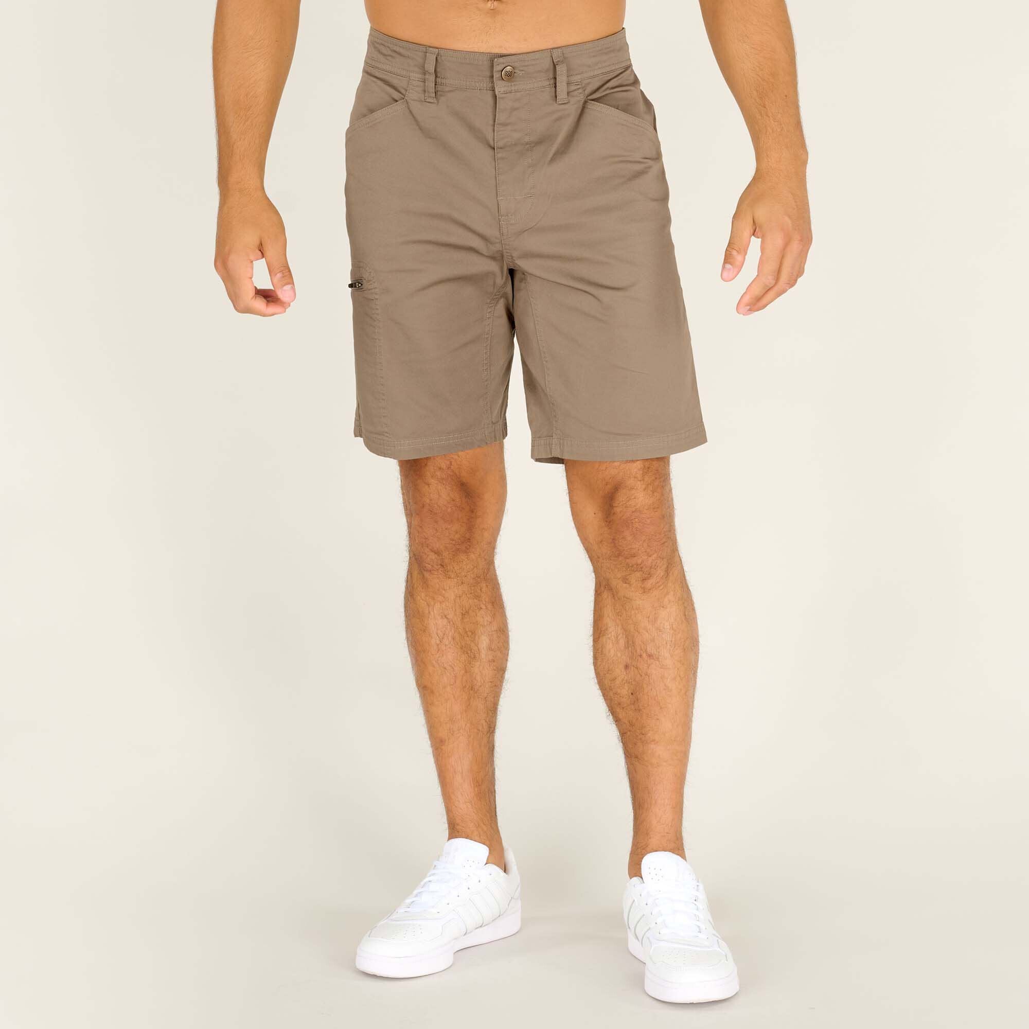 A pair of Sherpa Adventure Gear Tenjing Shorts in Grey displayed on a male model standing upright. The shorts have a classic fit, featuring belt loops, a button closure at the waistband, and slanted front pockets. The model is wearing white trainers.