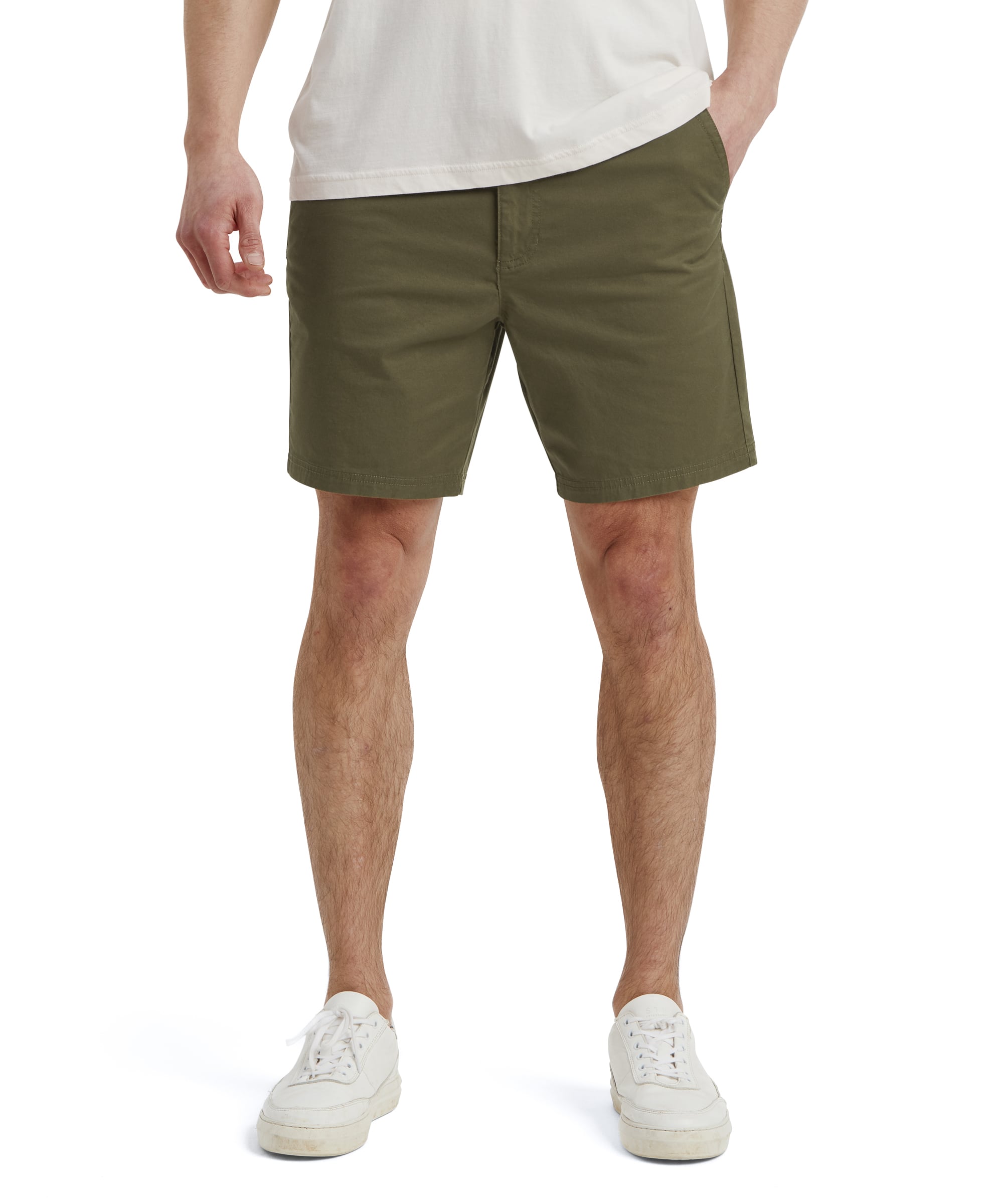 A front view of Sherpa Adventure Gear Tenjing Tour Shorts in Green worn by a model. The shorts reach above the knees and have a minimalistic design with a flat waistband, button closure, and front pockets. The model pairs them with a white t-shirt and white trainers, emphasising a clean and relaxed look.