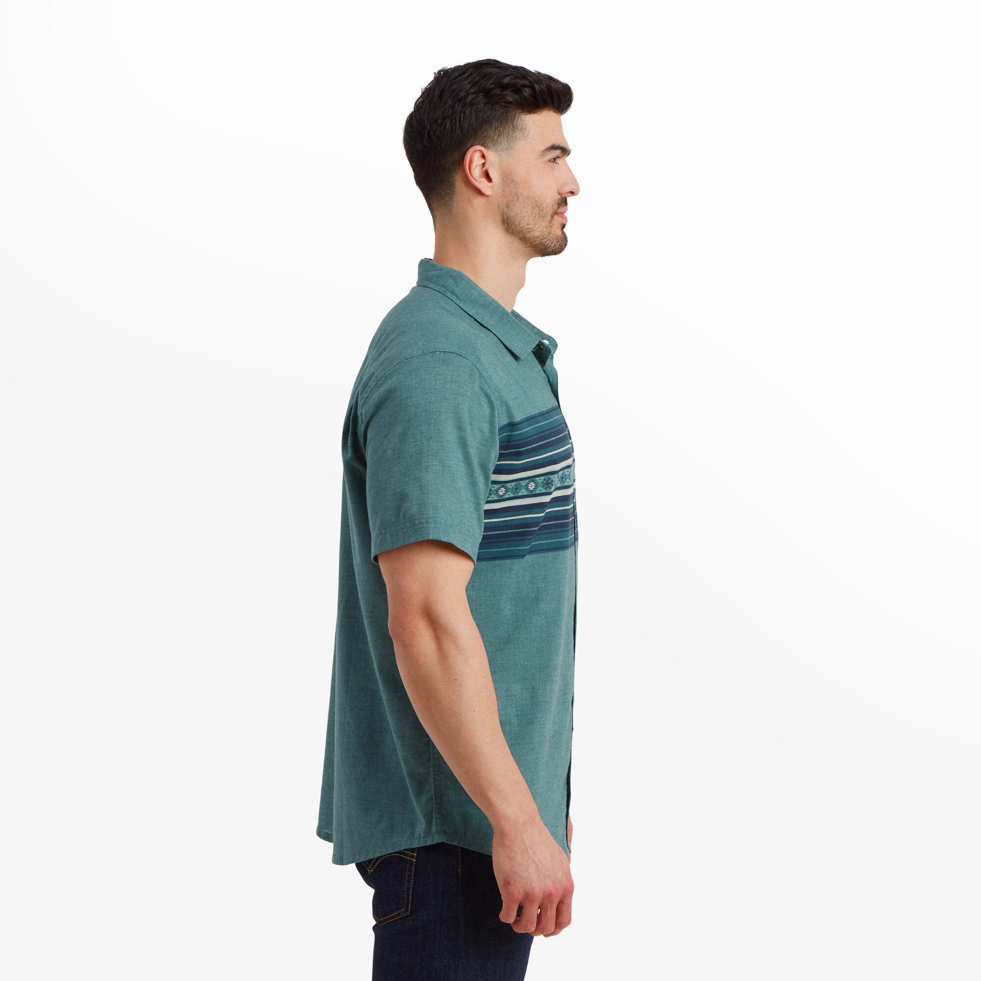 A side profile of the man wearing the Sherpa Adventure Gear Tibet Stripe Short Sleeve Shirt in Blue, showcasing its relaxed fit and the smooth, lightweight fabric. The model is positioned against a white background, highlighting the simple and clean design of the shirt.