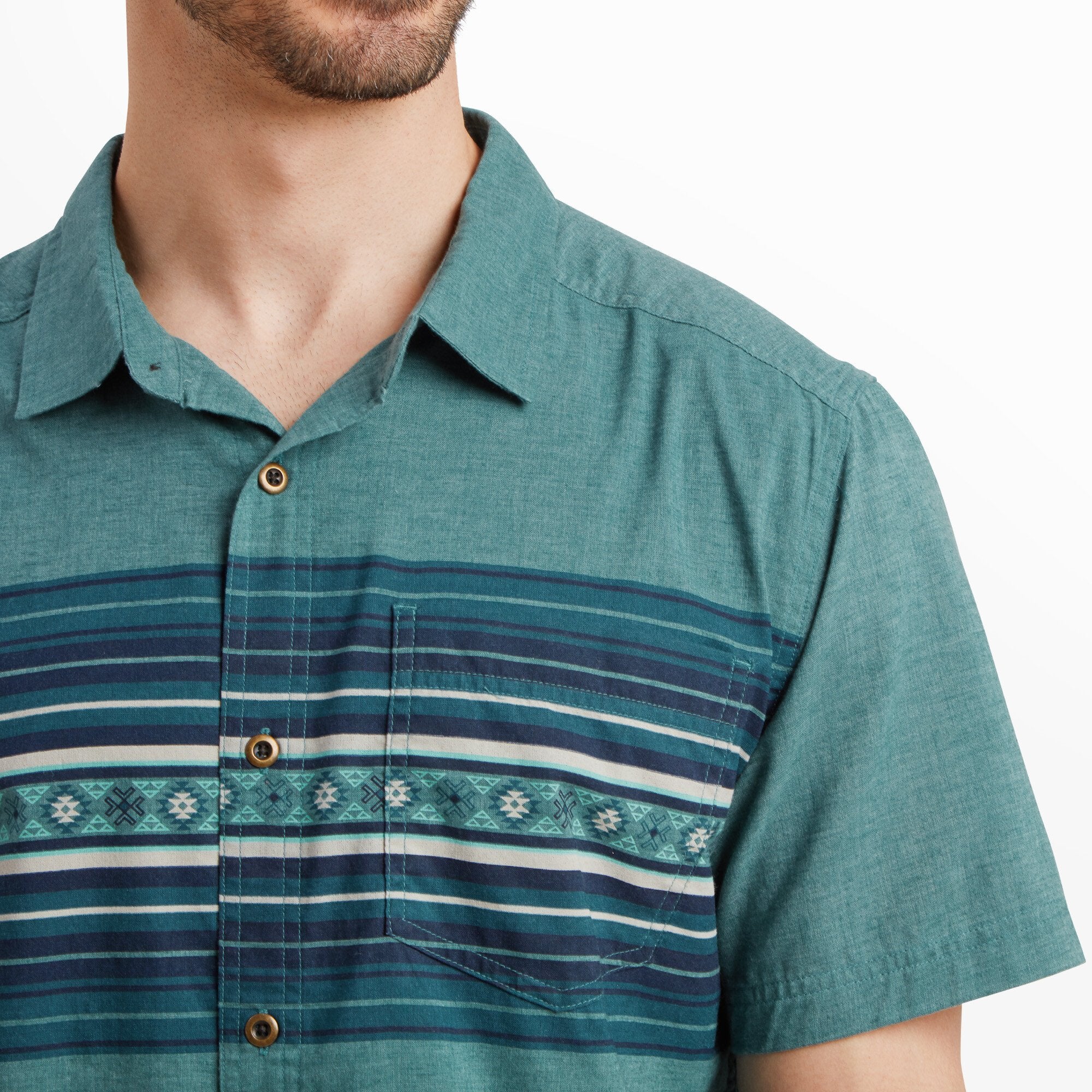 A close-up of the Sherpa Adventure Gear Tibet Stripe Short Sleeve Shirt in Blue's chest area, focusing on the intricate striped patterns and pocket detail. The button-up design is highlighted, with natural wood-like buttons complementing the shirt's casual style.