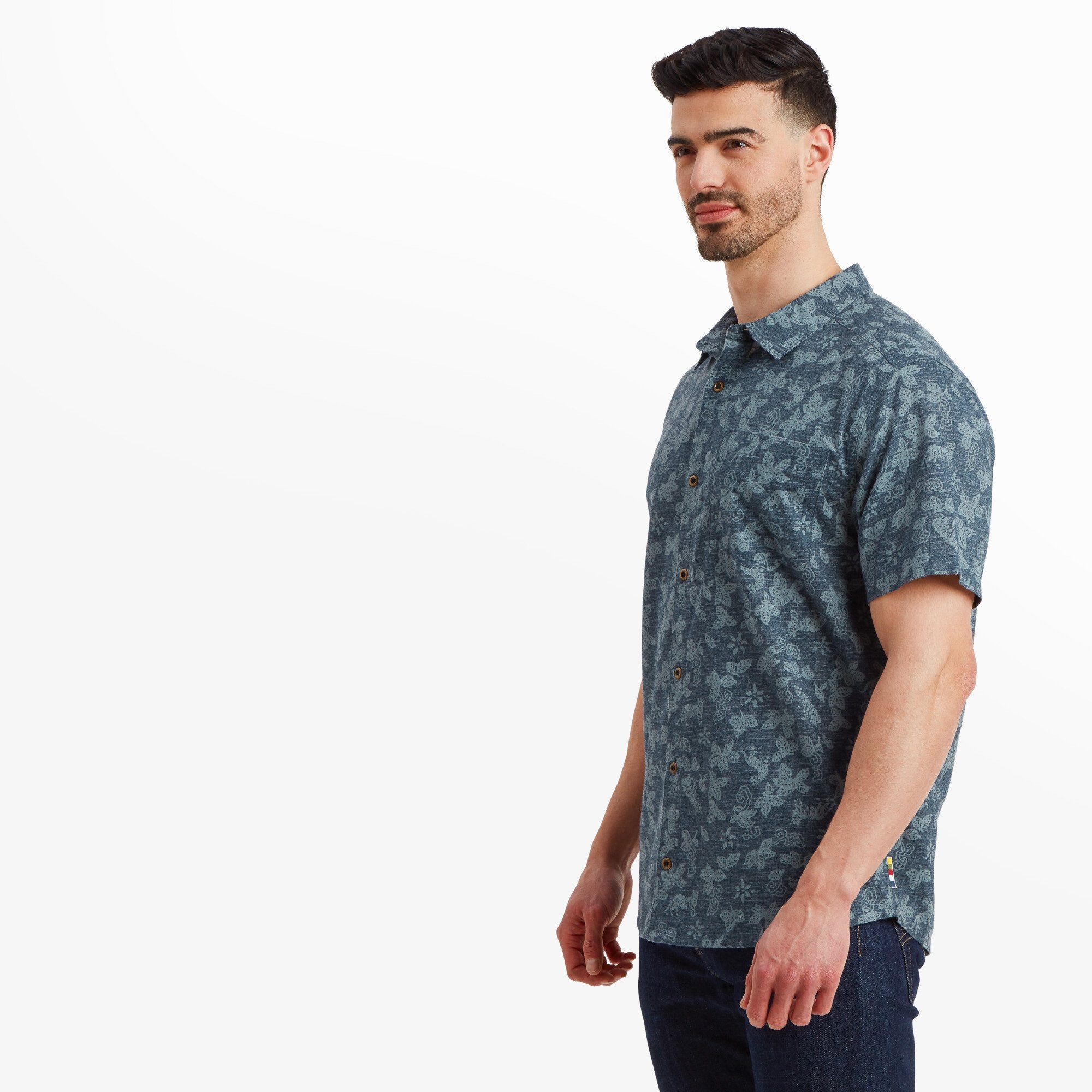 The same Sherpa Adventure Gear Tiger Floral Short Sleeve Shirt in Blue shown from a side angle. The model is facing slightly away, highlighting the smooth, tailored fit along the shoulders and arms. The shirt's intricate floral pattern is visible against the lightweight fabric.