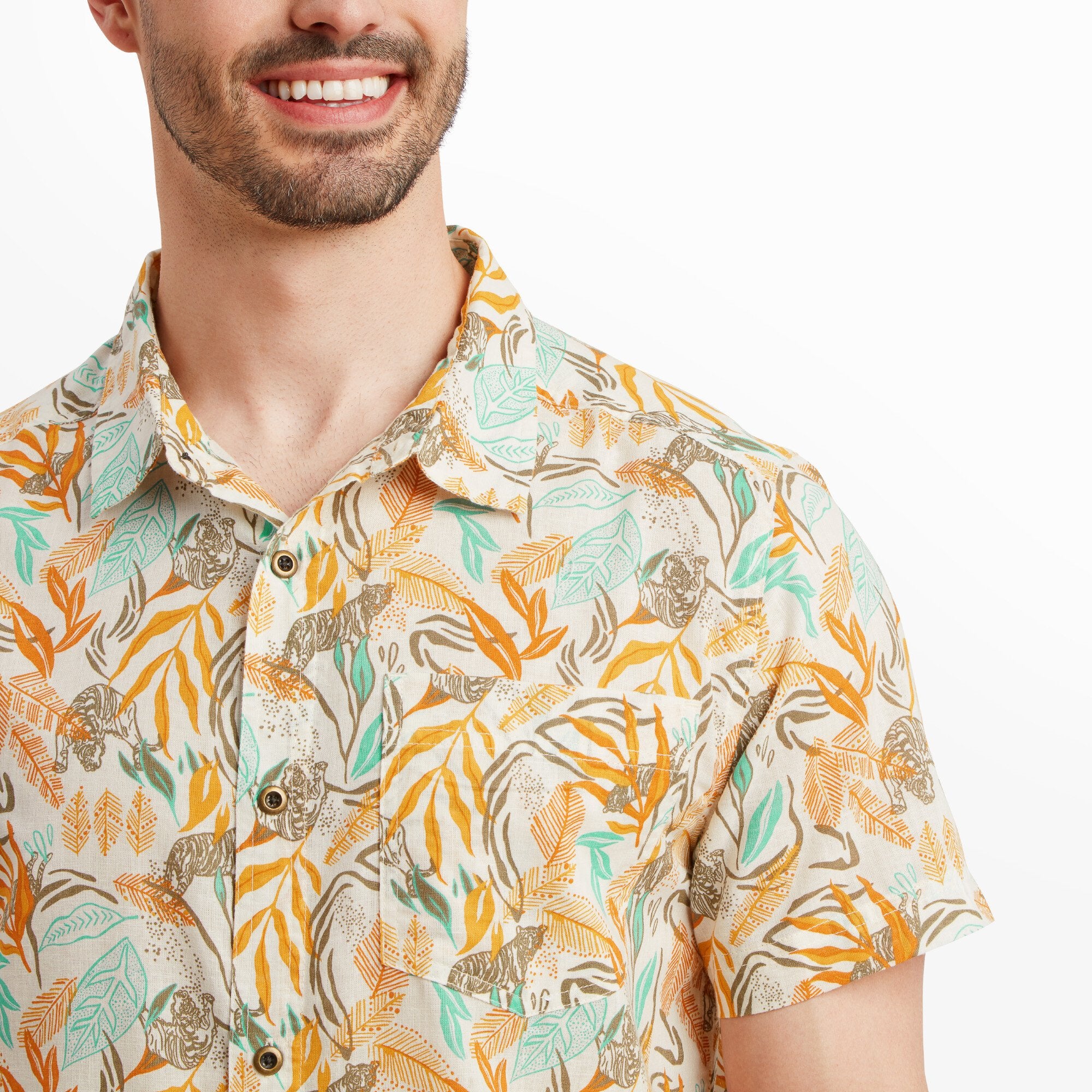 A detailed close-up of the Sherpa Adventure Gear Tiger Leaf Short Sleeve Shirt in Orange's front chest area, emphasising the intricate tropical leaf and tiger print in orange, beige, and green hues. The button details are visible, adding a touch of craftsmanship.