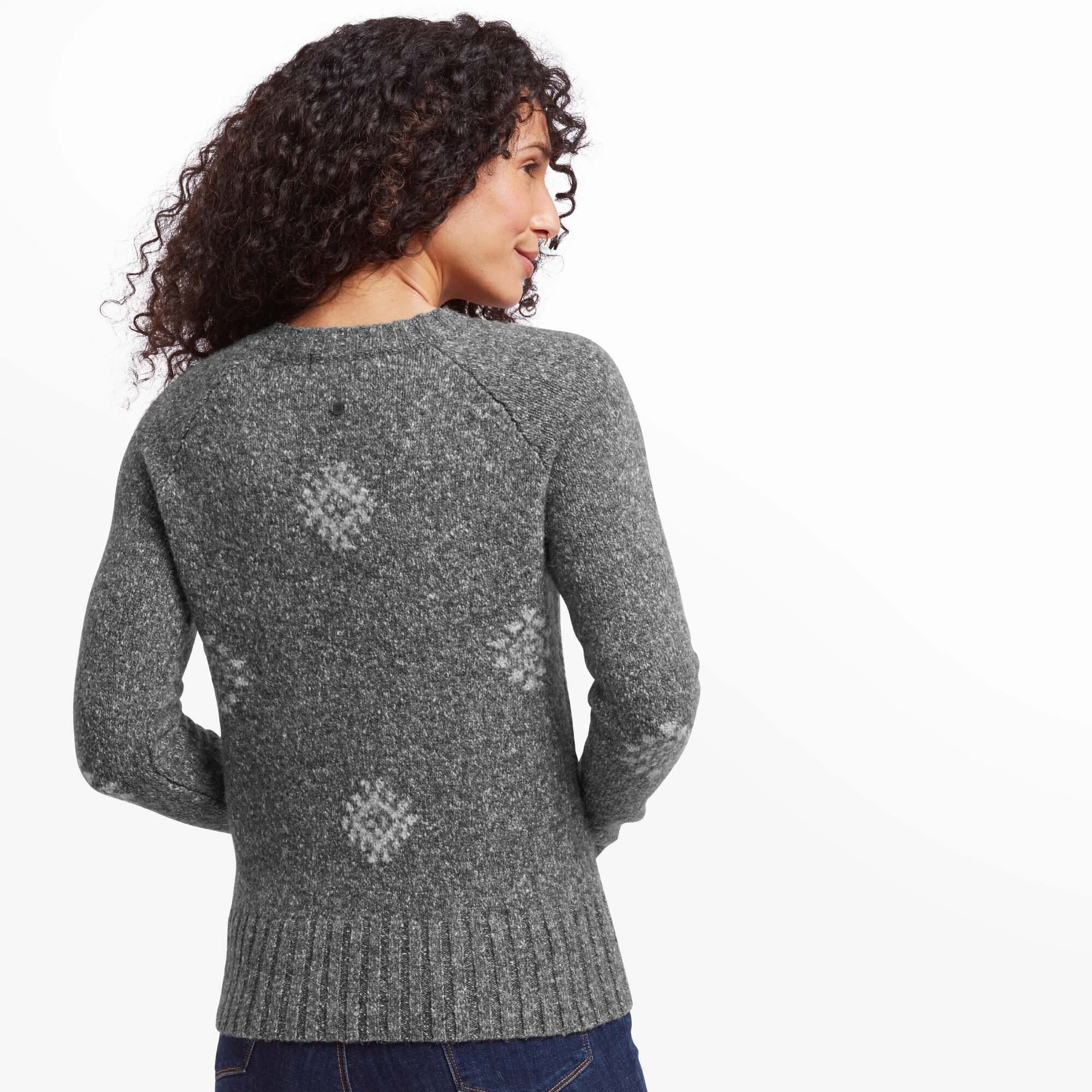 A rear view of the woman wearing the Sherpa Adventure Gear Vindo Crew in Grey, showcasing the pattern continuity on the back. The geometric snowflake design is evenly distributed, and the ribbed hem and cuffs are clearly visible, emphasising the attention to detail in the sweater's construction.