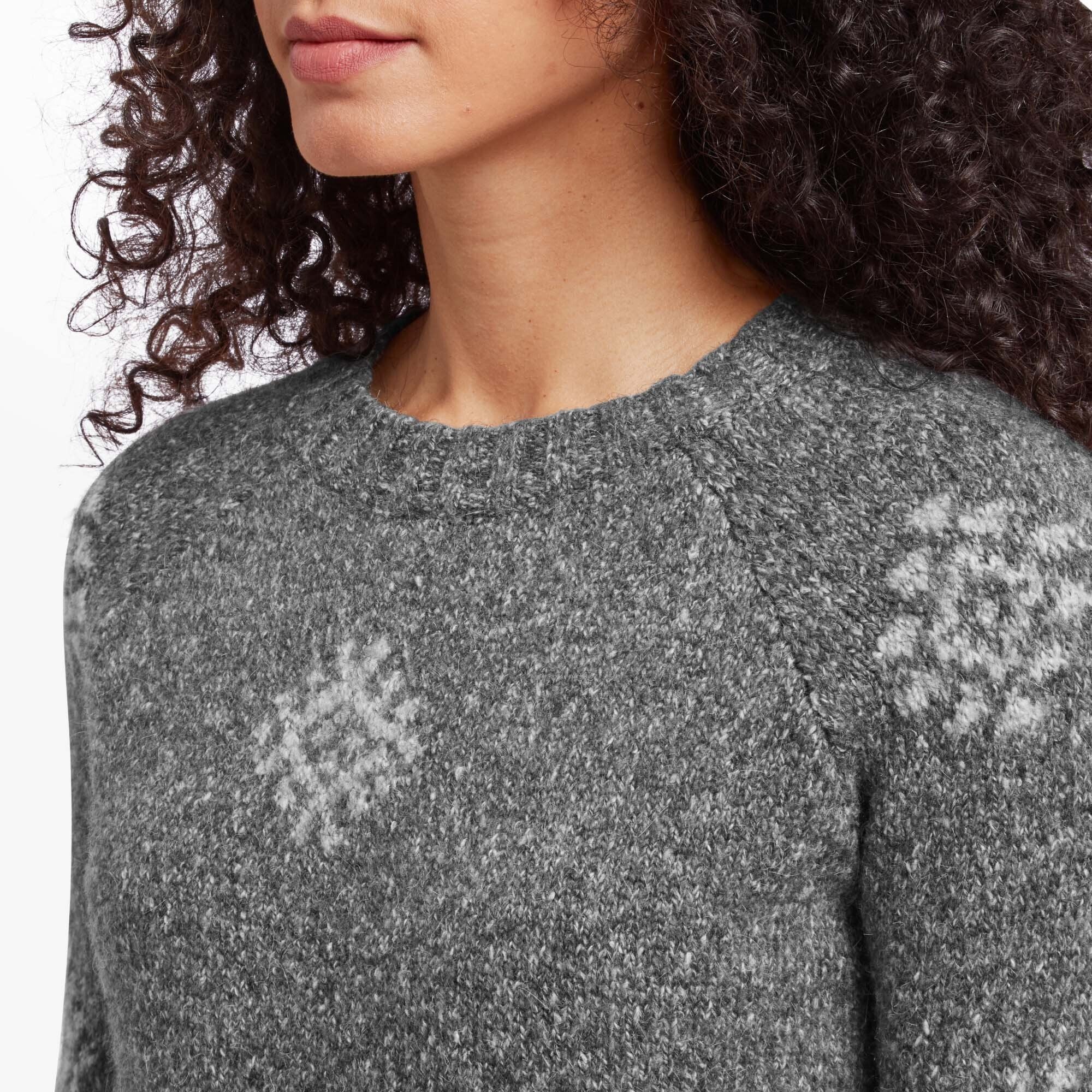 A close-up of the neckline and upper shoulder of the Sherpa Adventure Gear Vindo Crew in Grey. The fine knit texture is showcased alongside the delicate geometric snowflake patterns, demonstrating the sweater's quality and craftsmanship. The raglan sleeve design is subtly visible in the framing.