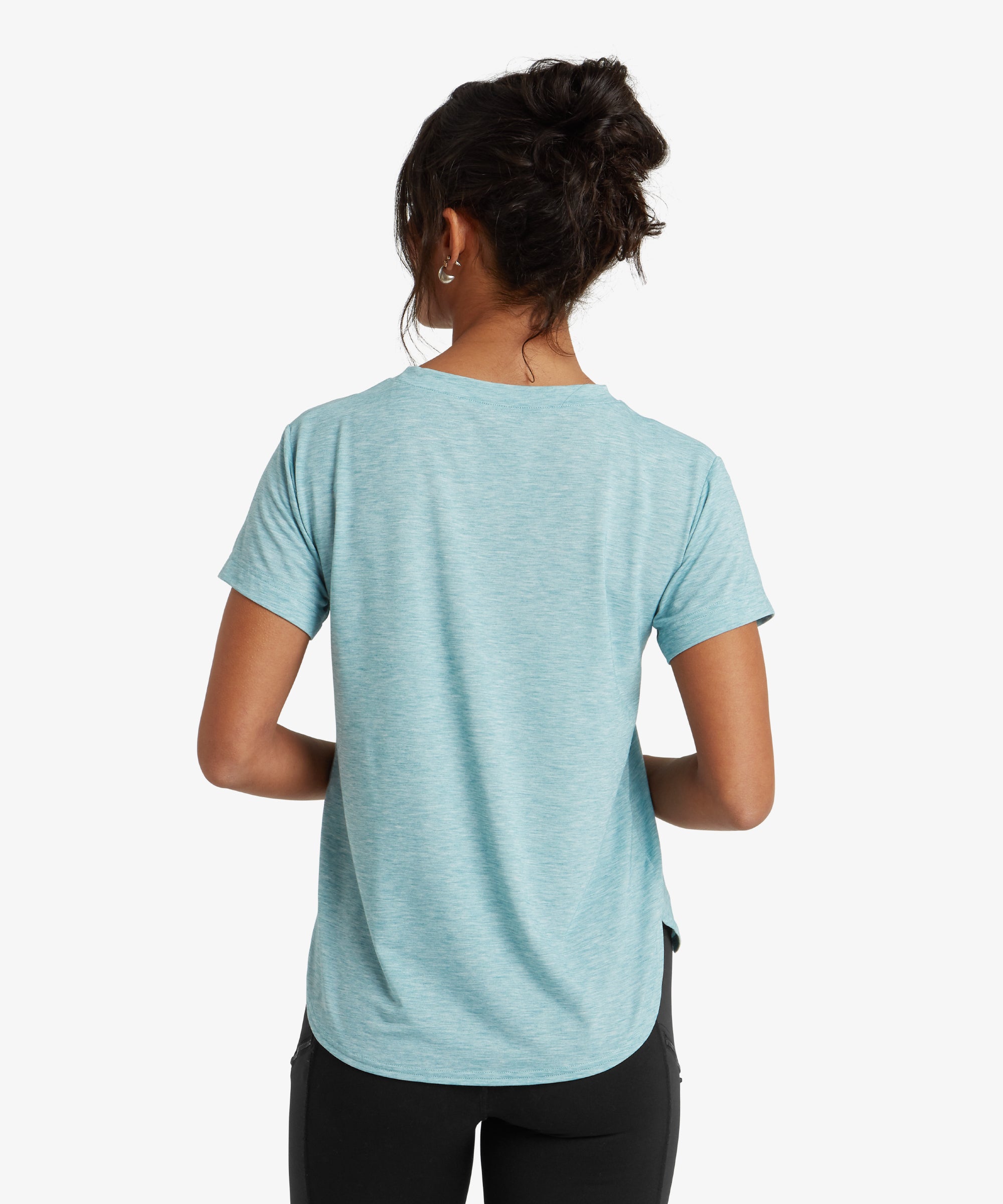 A detailed close-up of the Sherpa Adventure Gear Asha Crew in Blue's neckline and fabric texture. The crew neck is neatly stitched, and the light blue fabric shows a subtle heathered pattern, indicating a soft, breathable material. The model's delicate necklace complements the minimalistic style of the T-shirt.