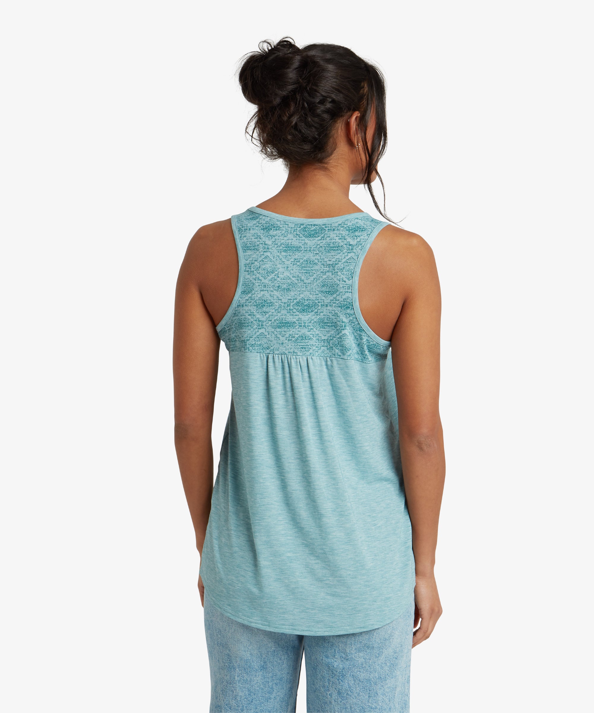 The rear view of the Sherpa Adventure Gear Asha Tank in Blue shows a racerback design with a unique patterned fabric on the upper back panel. The pattern consists of intricate geometric details, adding a stylish accent to the otherwise simple top. The back hemline is slightly longer, providing extra coverage.