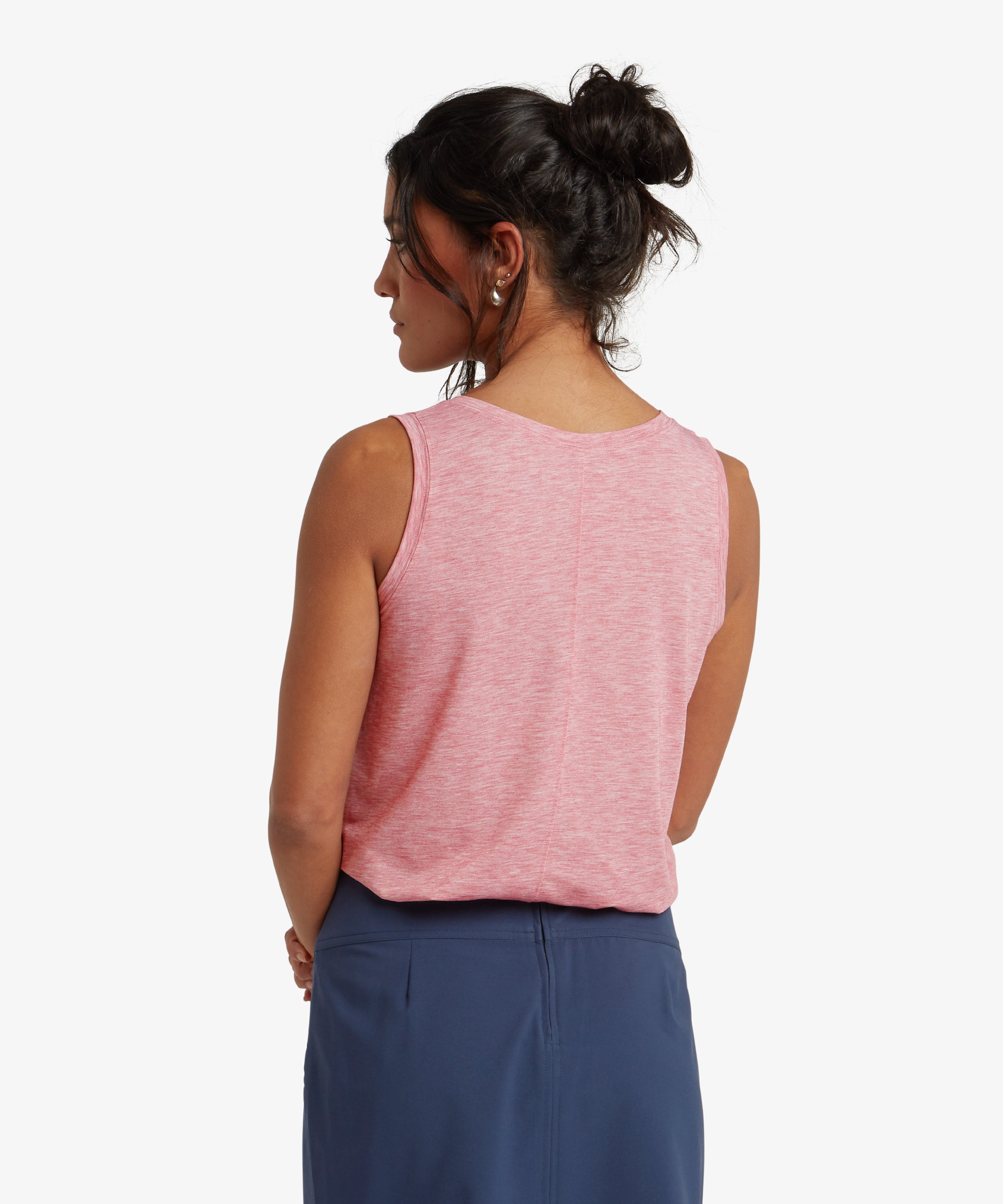 A full back view of the woman highlights the Sherpa Adventure Gear Asha V-Neck Tank in Red’s straight cut and the center seam running vertically down the back. Her hair remains tied up, revealing the soft, comfortable fabric of the top. The white background enhances the details of the garment.