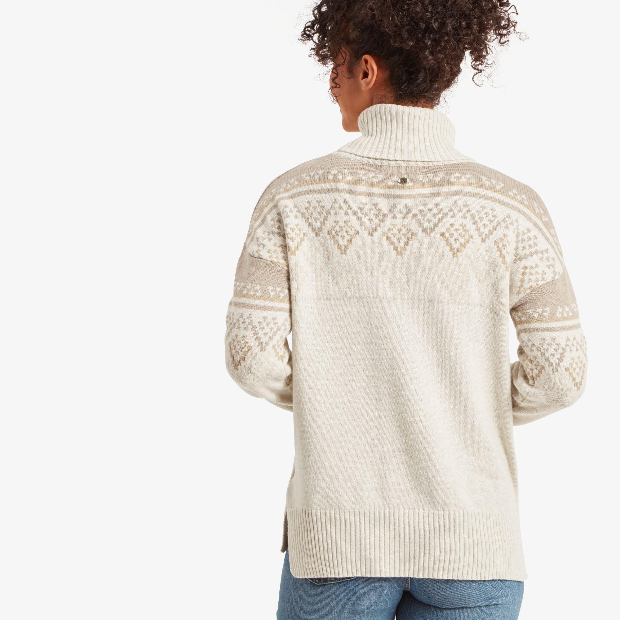 A view of the same Sherpa Adventure Gear Azha Roll Neck Sweater in White from the back, showcasing the fair isle design across the shoulders and upper back. The ribbed hem at the bottom and the rolled neck are clearly visible. Her curly hair is tied up, allowing the details of the sweater's back to be highlighted.