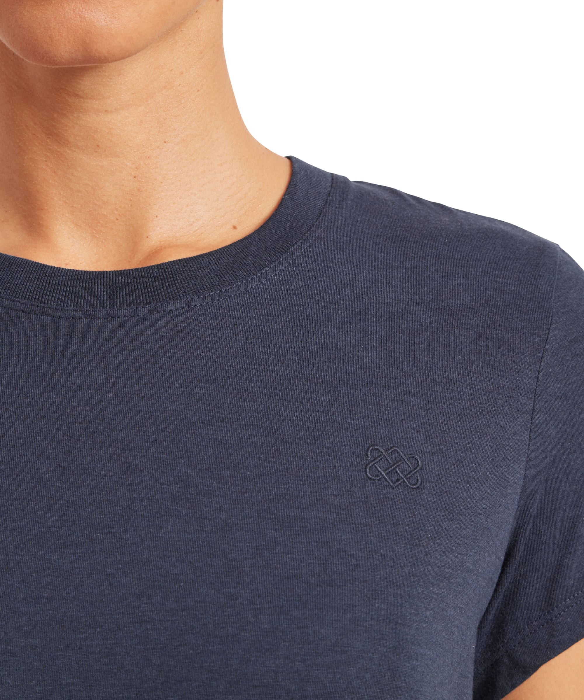 A detailed view of the left chest area of the Sherpa Adventure Gear Bali T-Shirt in Blue, showing the small Sherpa logo embroidered in a matching navy tone. The fabric texture is slightly visible, highlighting the quality and craftsmanship of the shirt.