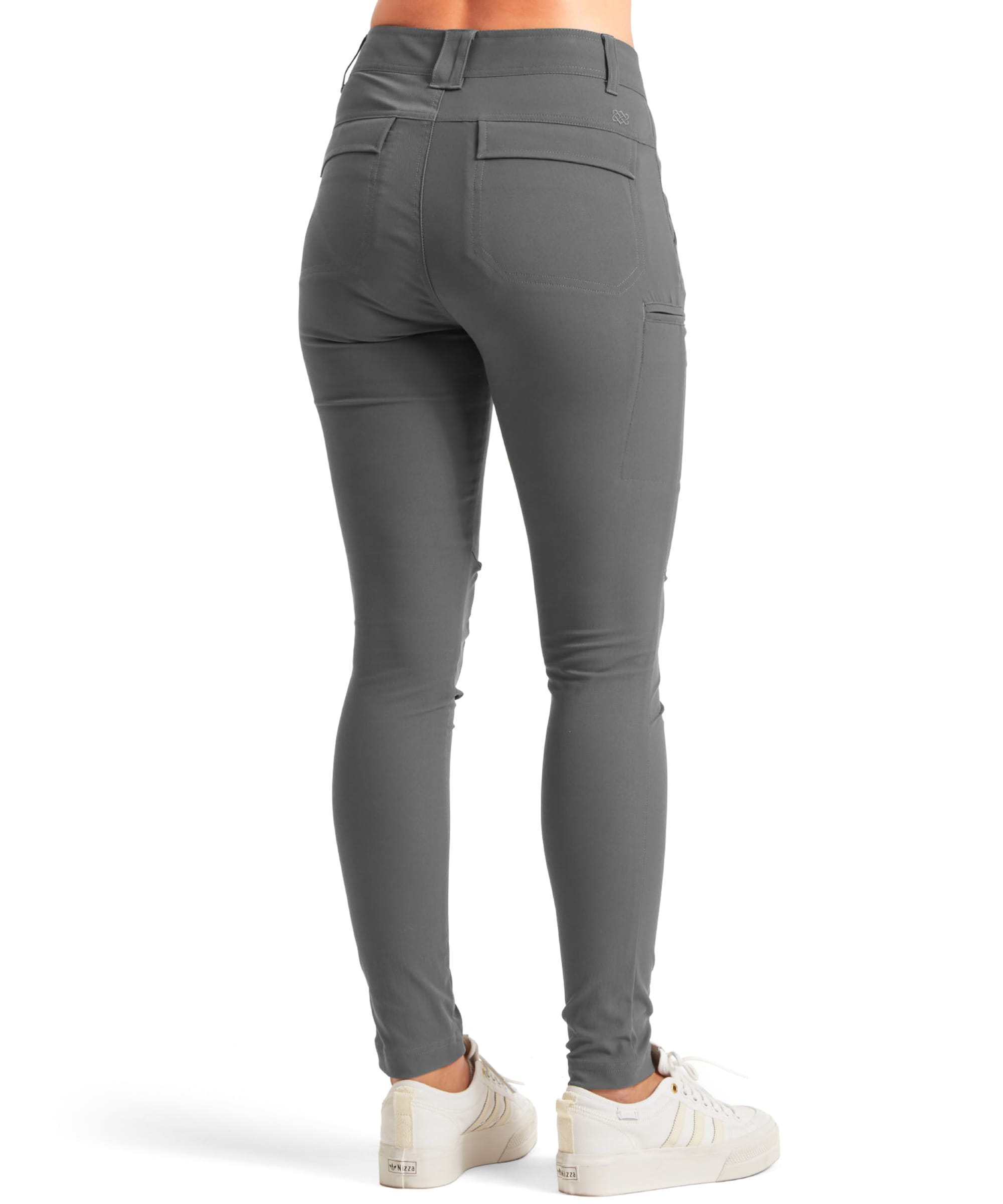 Back view of the Sherpa Adventure Gear Bara Tapered trousers in Grey showing the flattering fit and practical details such as two rear patch pockets. The trousers hug the legs with a slight tapering at the ankle. The model pairs the trousers with white trainers for a casual look.