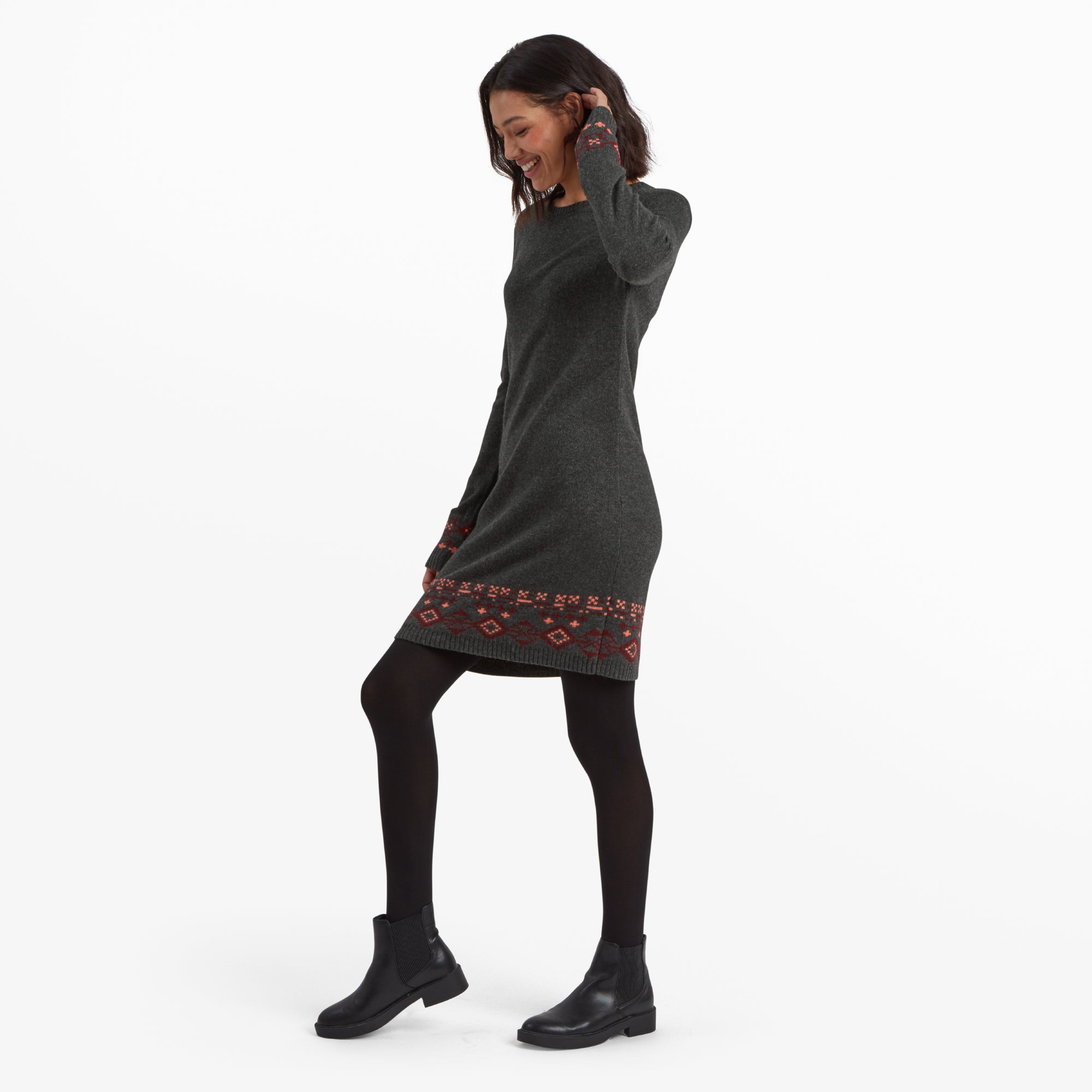 A side profile of the woman in the Sherpa Adventure Gear Bharati Eco Dress in Grey, showing the slim, tailored fit and highlighting the intricate geometric pattern near the hem. She has one hand brushing her hair.