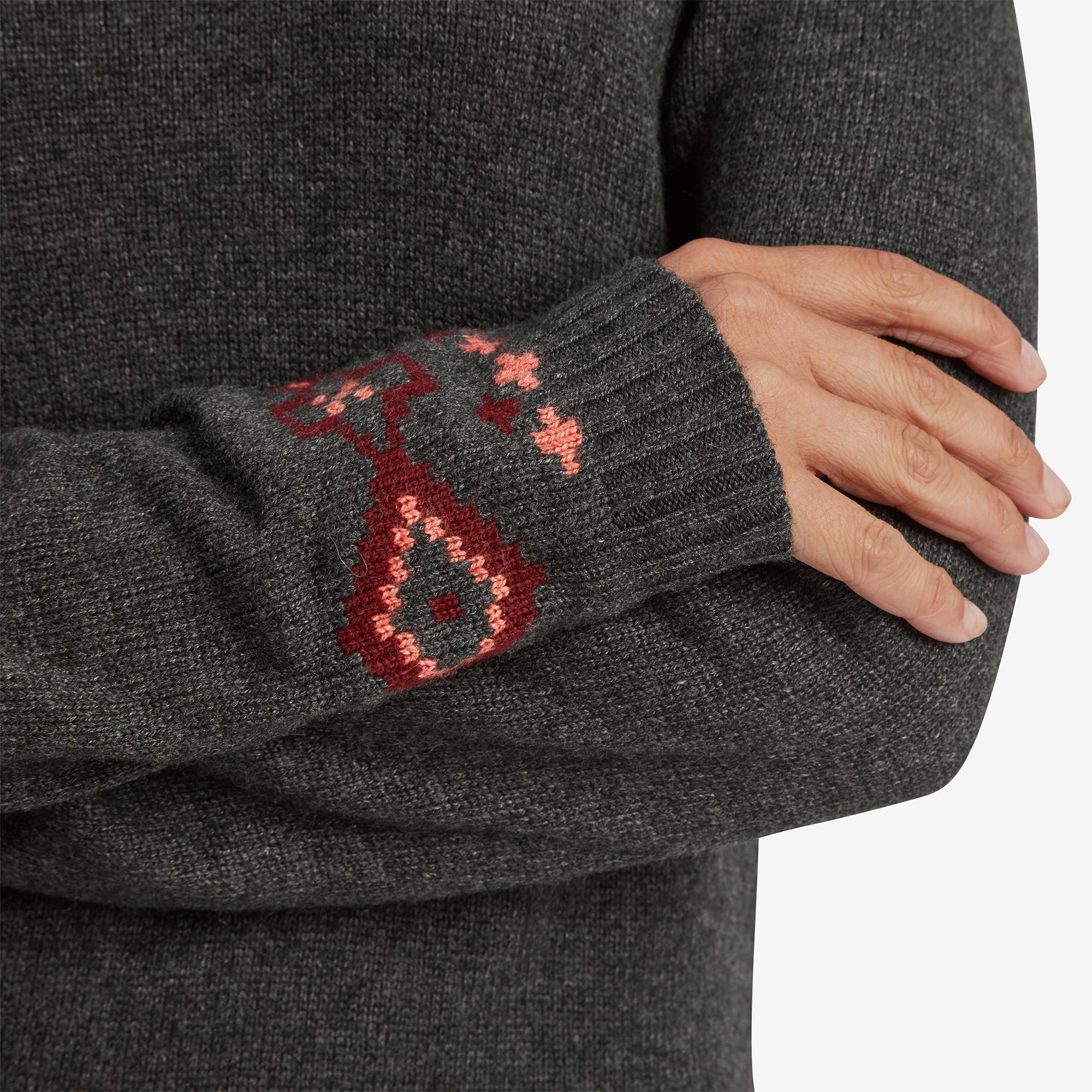 A close-up of the cuff of the Sherpa Adventure Gear Bharati Eco Dress in Grey sleeve, showing detailed red and pink geometric patterns knitted into the ribbed fabric.