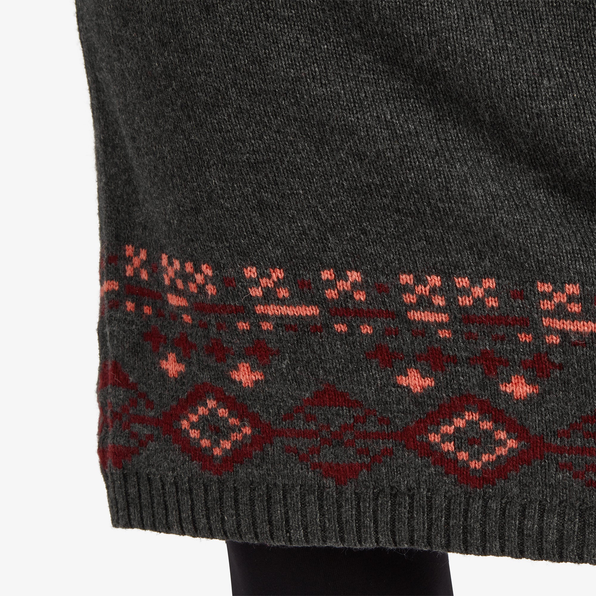 A close-up of the hem of the Sherpa Adventure Gear Bharati Eco Dress in Grey, showcasing the rich geometric design in red and pink tones against the grey fabric, emphasising the craftsmanship and texture.