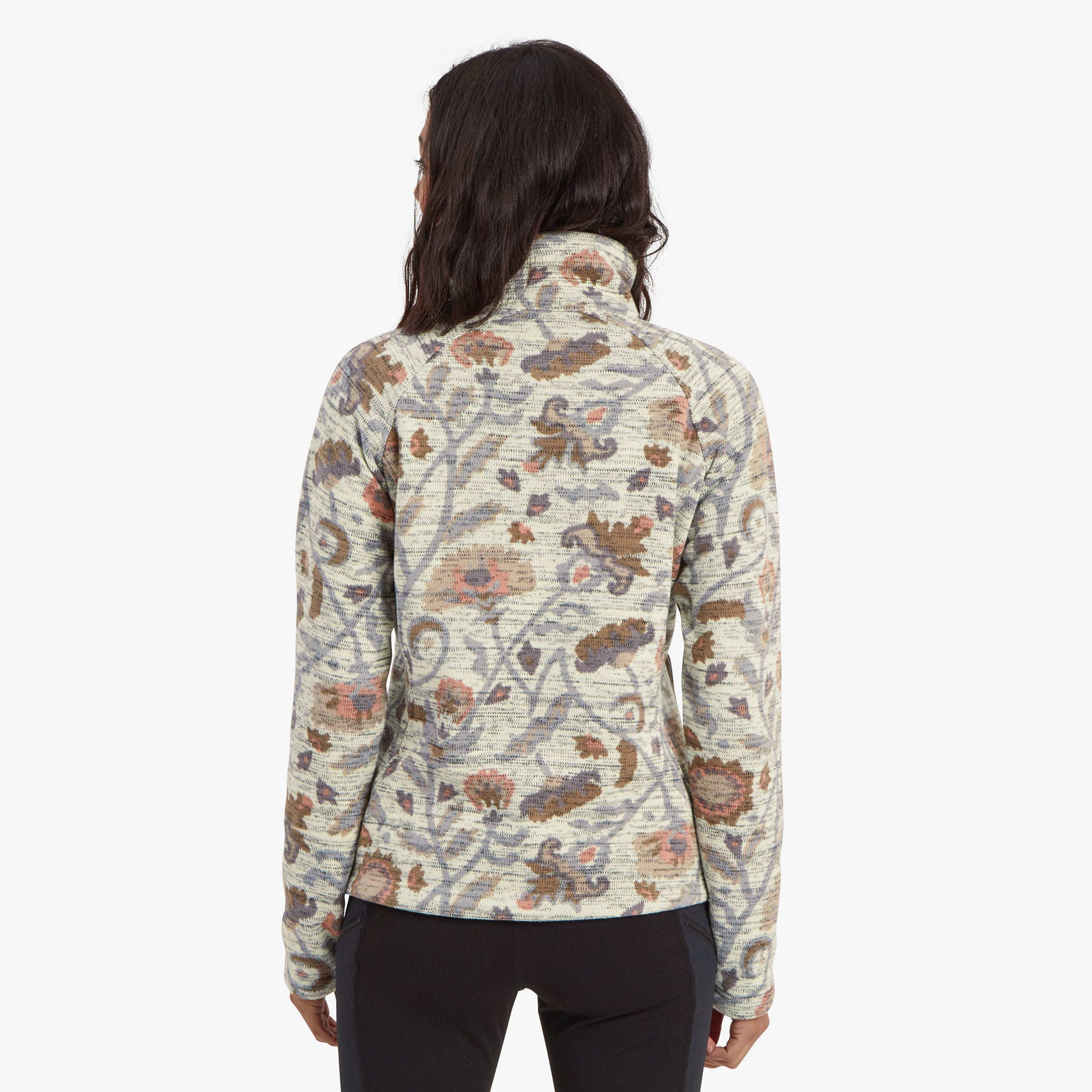 The model is turned away, displaying the back of the Sherpa Adventure Gear Bhutan Pullover in Light Brown. The floral-inspired pattern extends across the entire back, showcasing the seamless design continuity. The fit is relaxed, with a slightly curved hemline that adds a feminine touch. The pullover’s texture is subtly visible, enhancing its cozy aesthetic.