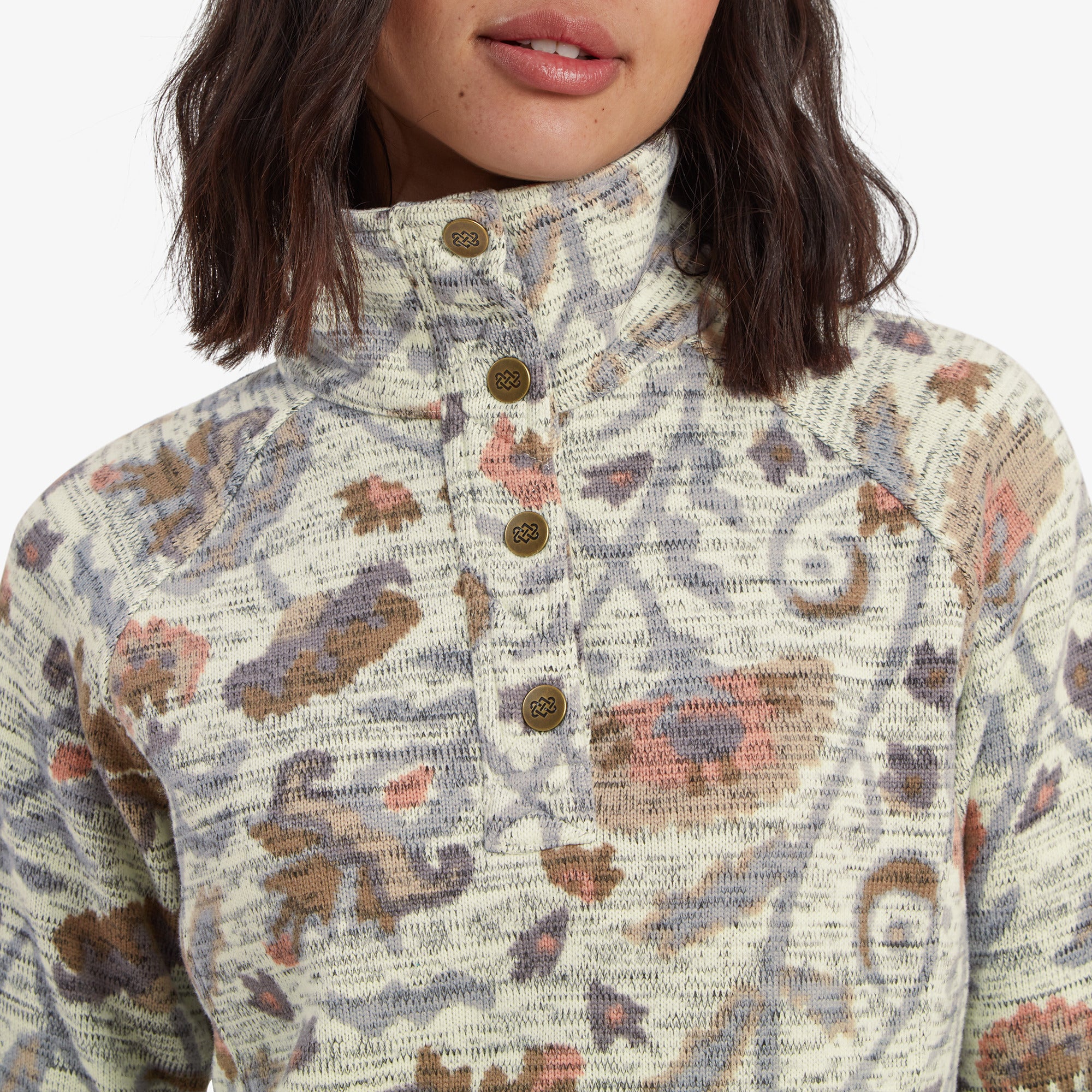 A detailed shot of the high-neck collar of the Sherpa Adventure Gear Bhutan Pullover in Light Brown, emphasising the textured knit fabric and the four small round buttons on the placket. Each button has a subtle engraved design, adding a decorative element. The floral pattern is more vivid in this close-up, with soft hues blending harmoniously.