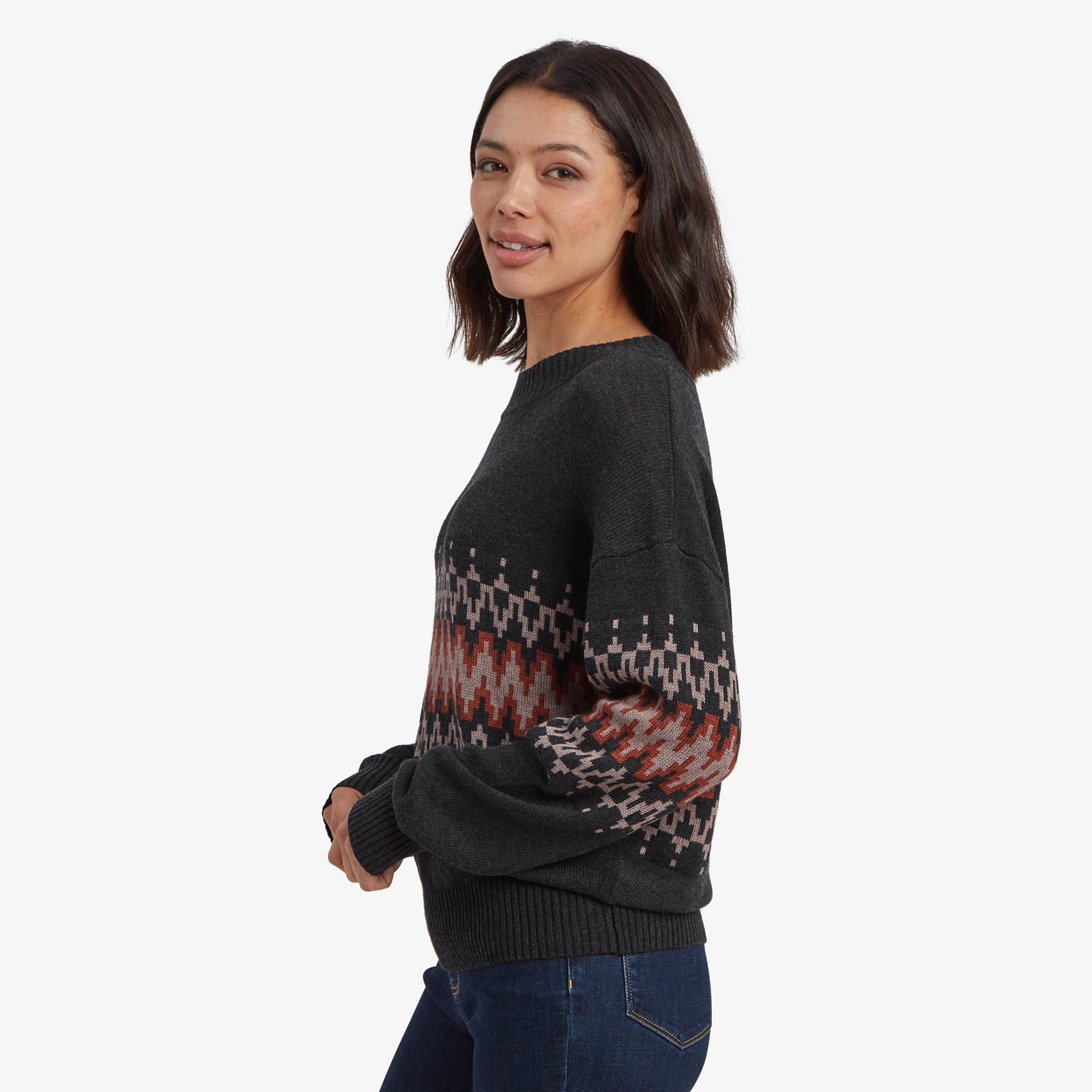 A side profile view of the model wearing the Sherpa Adventure Gear Devaki Eco Crew in Black, highlighting the dropped shoulder design and the detailed knit pattern extending across the sleeves and chest. The loose, cozy fit is clearly visible, as well as the ribbed cuffs and hem.