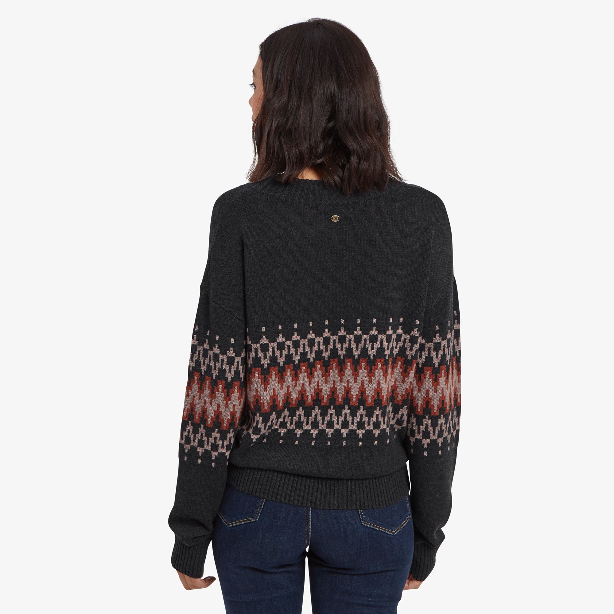 The back view of the model in the Sherpa Adventure Gear Devaki Eco Crew in Black, showing the continuation of the geometric design across the upper back and sleeves, while the lower part remains solid dark grey. The small brand emblem detail is also visible at the back neckline.