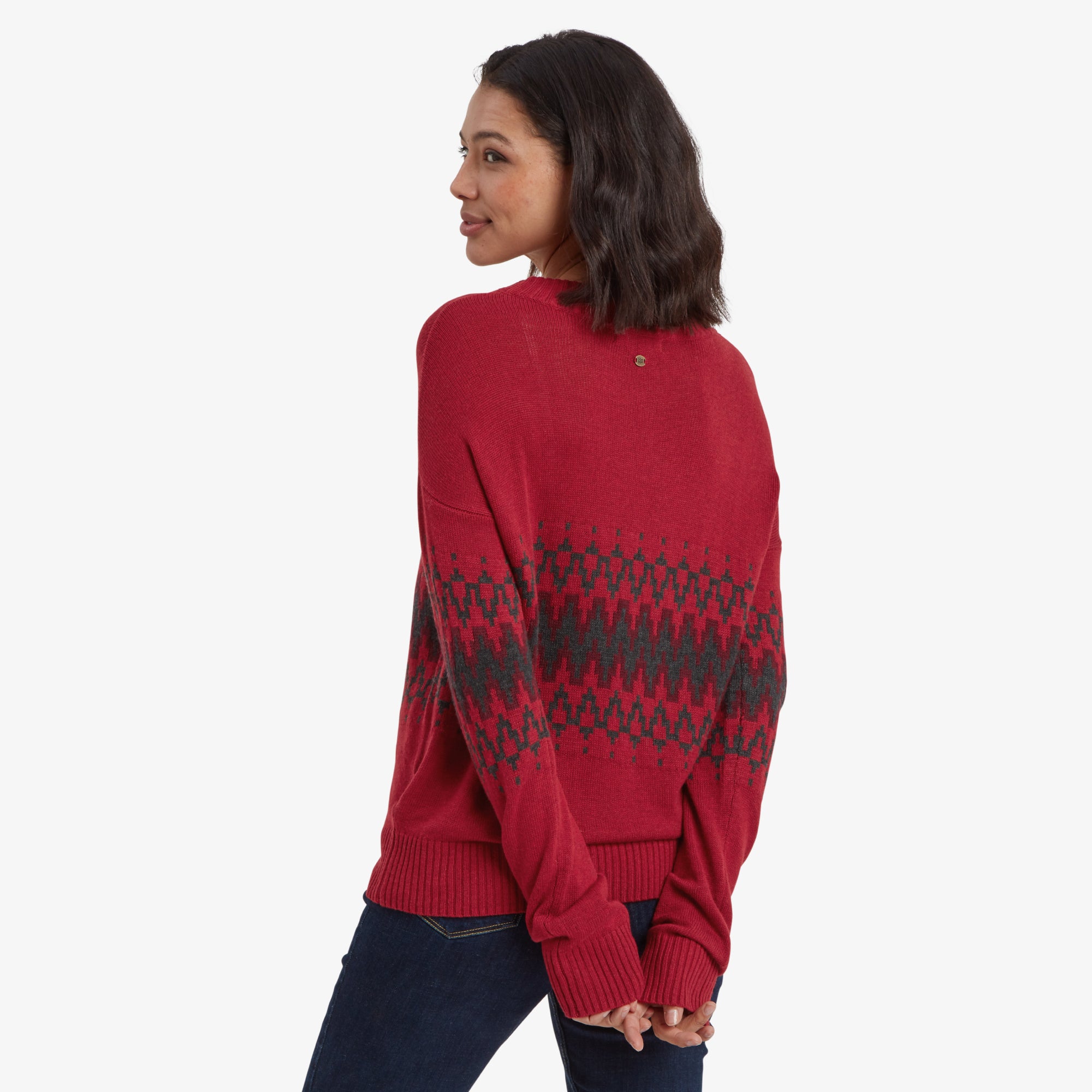 A rear view of the woman wearing the Sherpa Adventure Gear Devaki Eco Crew Sweater in Red. The black geometric pattern wraps around the back, blending seamlessly with the design on the front and sleeves. The ribbed hem and cuffs are visible, adding a clean finish to the garment.