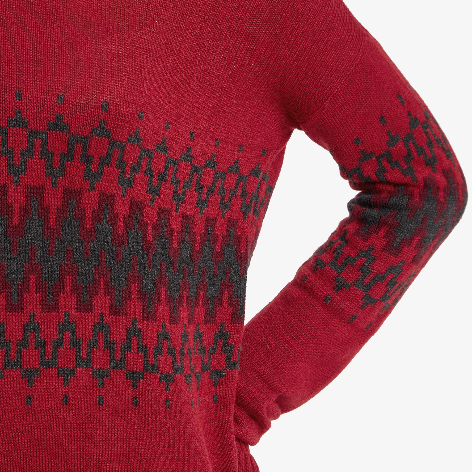 A close-up of the sleeve and chest area of the Sherpa Adventure Gear Devaki Eco Crew Sweater in Red, focusing on the intricate black geometric pattern. The pattern contrasts elegantly with the red base, emphasising the high-quality craftsmanship of the knit design.