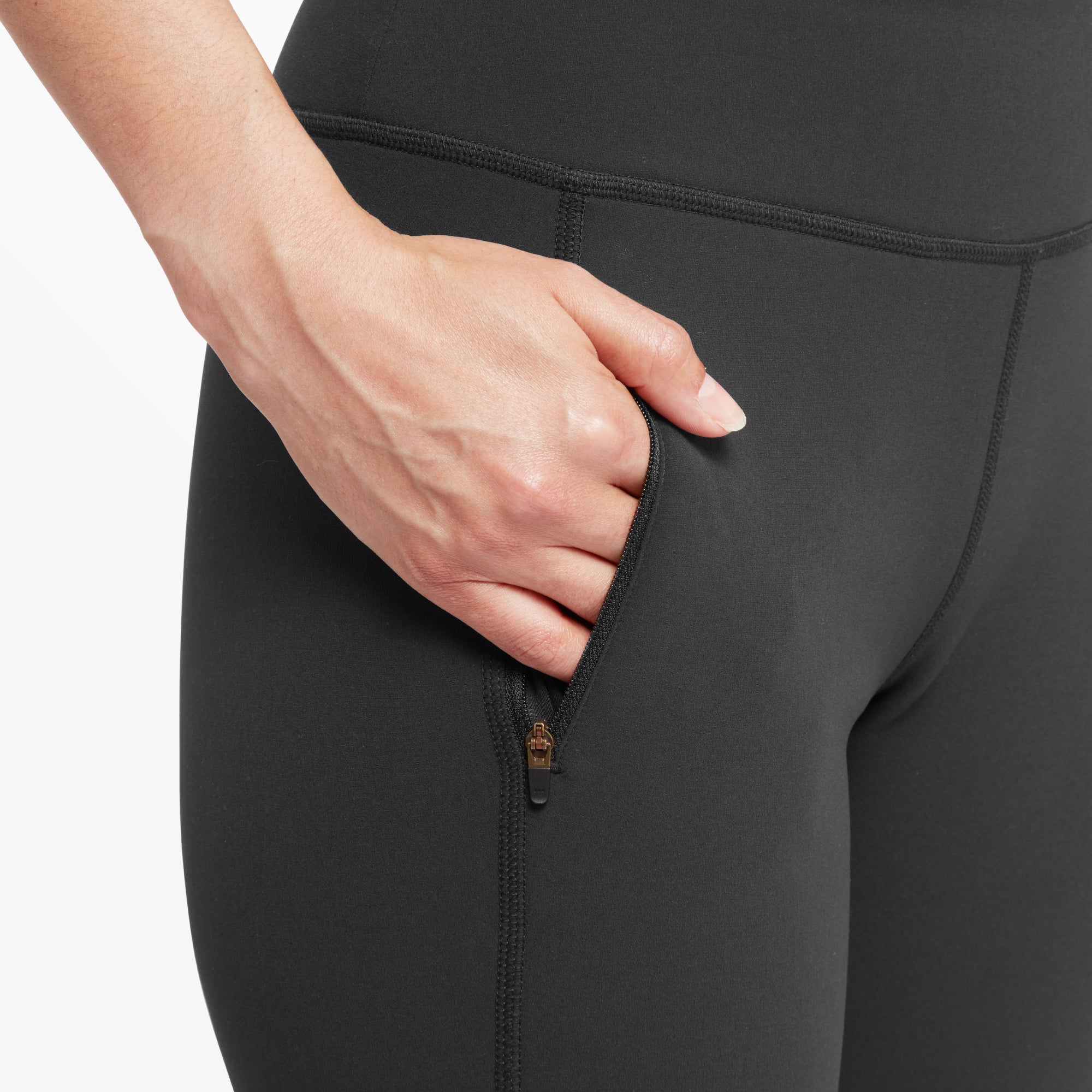 A close-up of the side pocket on the Sherpa Adventure Gear Dolma Softshell Tight in Black, slightly unzipped, revealing a black interior lining. The smooth fabric and precise stitching highlight the leggings' high-quality craftsmanship.