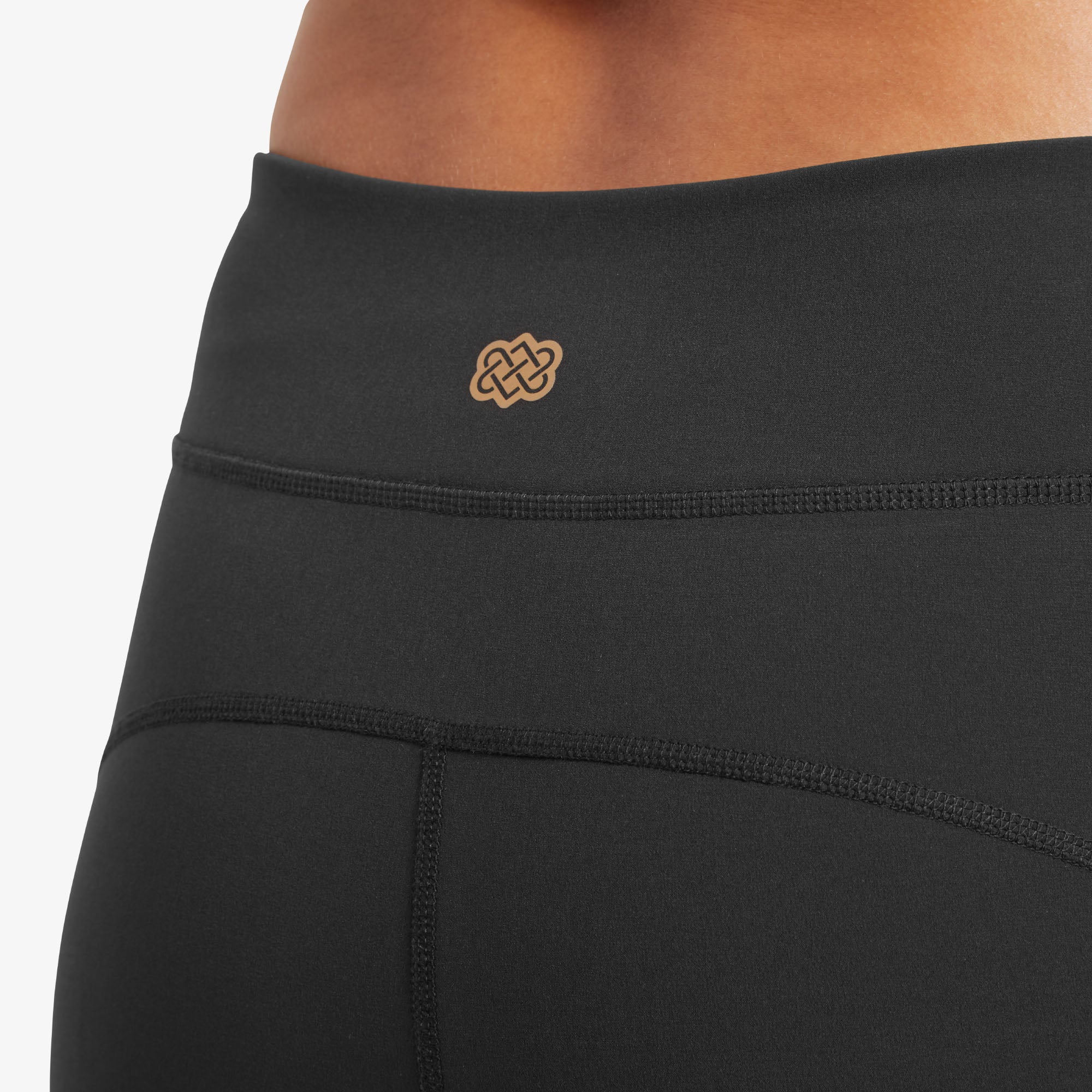 A detailed view of the back waistband of Sherpa Adventure Gear Dolma Softshell Tight in Black. The center of the waistband features a small, golden Sherpa Adventure Gear logo, subtly embossed. The stitching and fabric are shown in high detail, emphasising the sleek and seamless design.