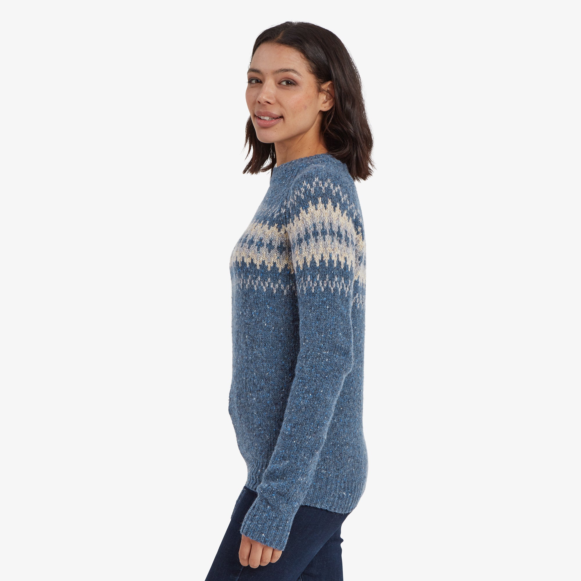 A side profile of the model wearing the Sherpa Adventure Gear Dumji Crew Sweater in Blue, emphasising its slightly tapered fit around the waist. The sweater's textured knit material is noticeable, and the Nordic pattern continues seamlessly across the shoulder area.